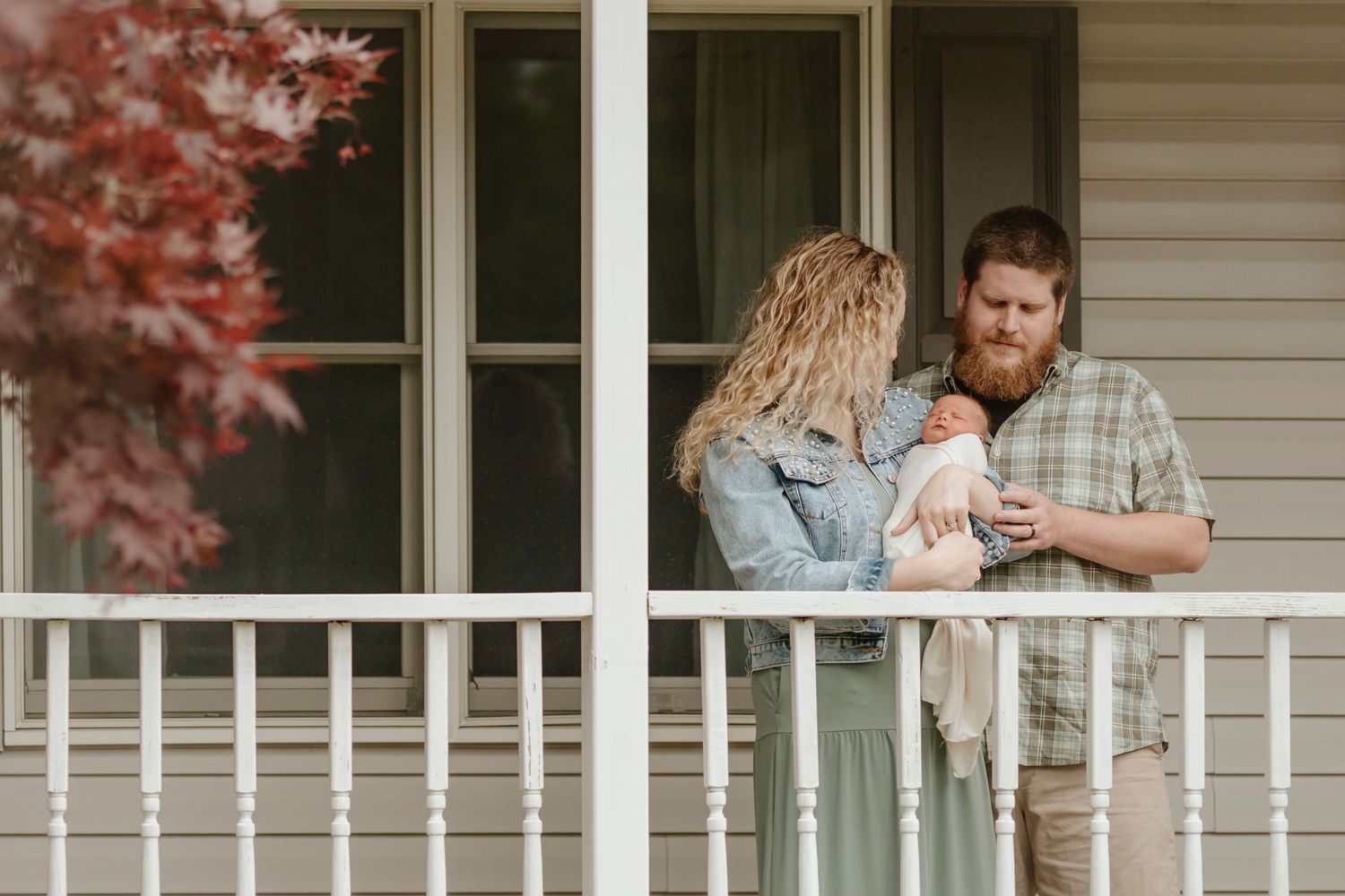 A family shares an intimate moment on their front porch with autumn foliage in the background.