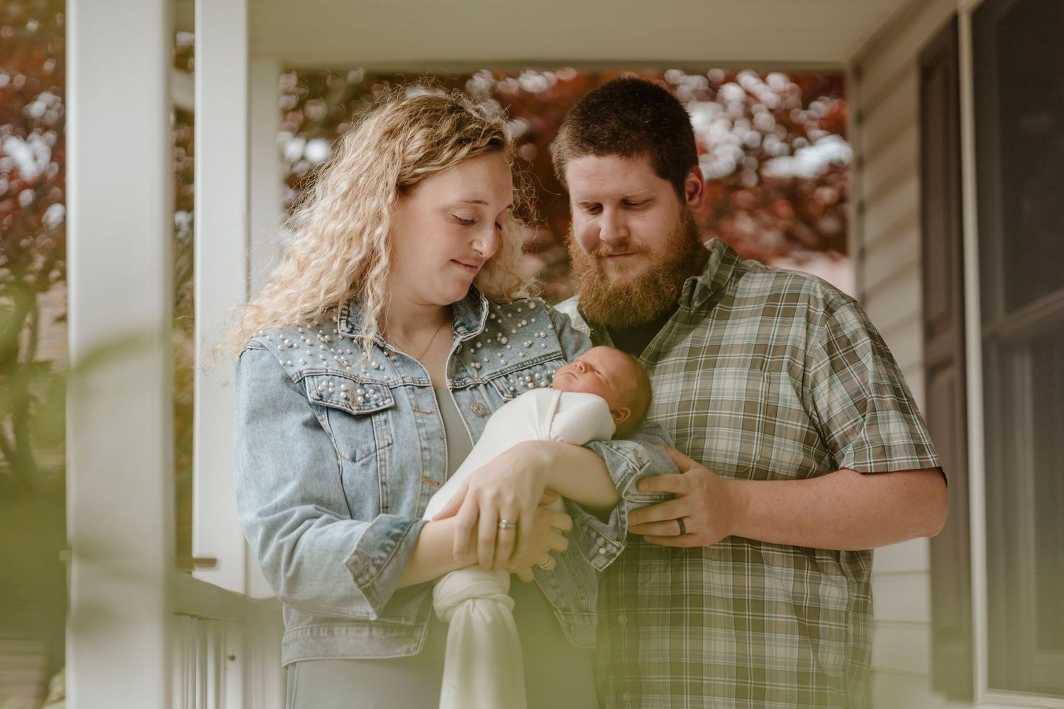 A couple shares a tender moment with their newborn on a front porch.