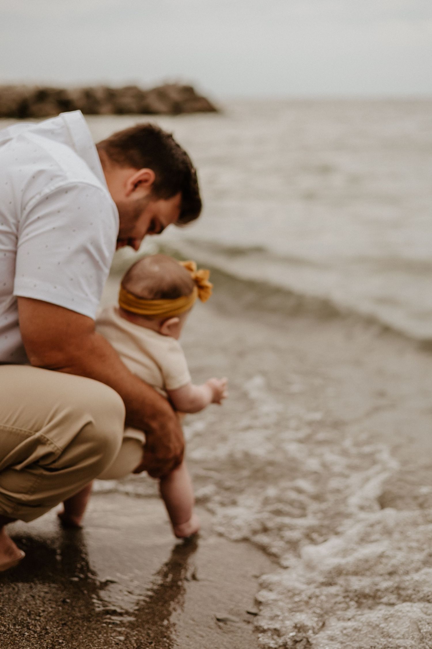 Parent and baby exploring the water's edge on a sandy beach.