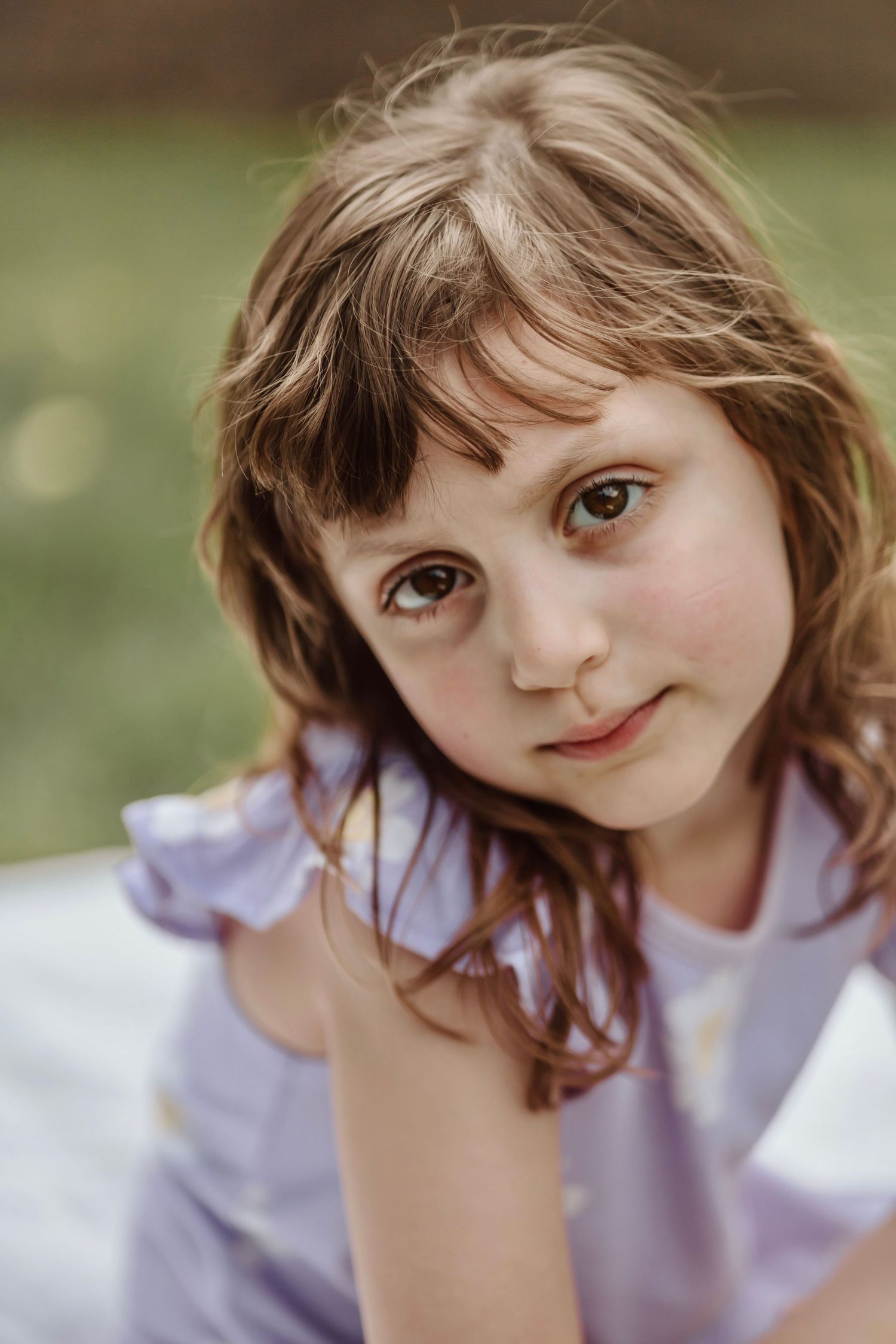Child in a lilac dress sitting outdoors with natural lighting and soft bokeh background.
