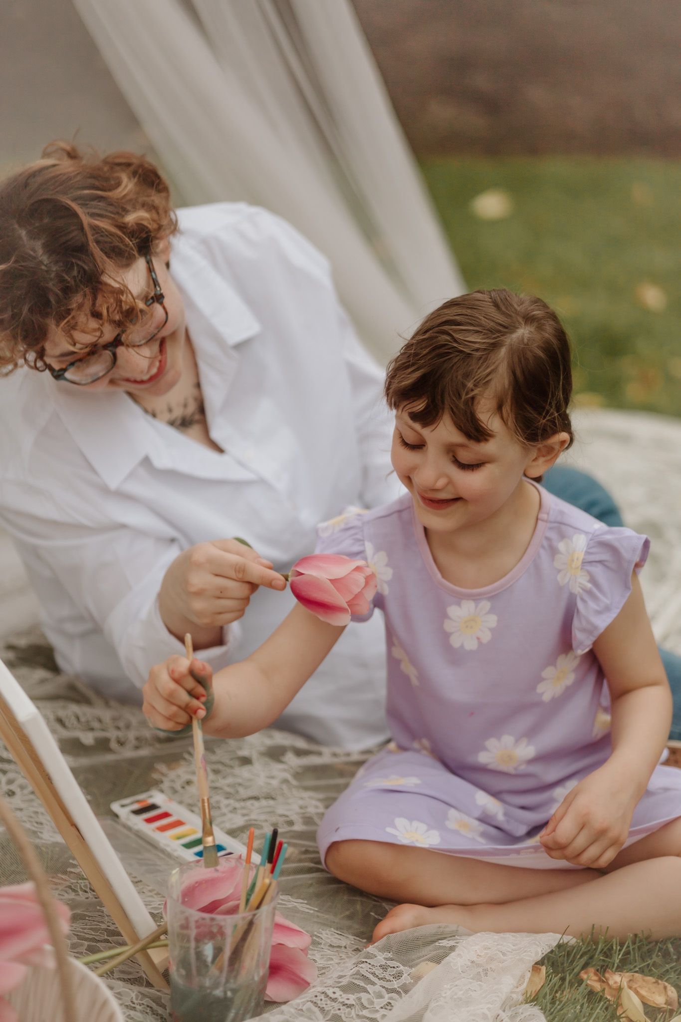 Parent and child painting together during an outdoor art session with pink flowers nearby.
