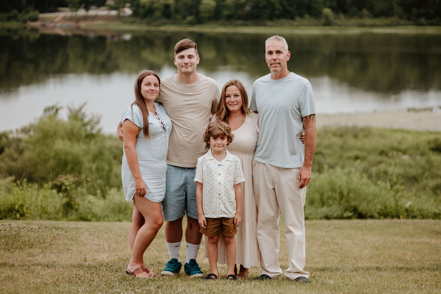 Family of five poses together on grassy hill with lake in background.