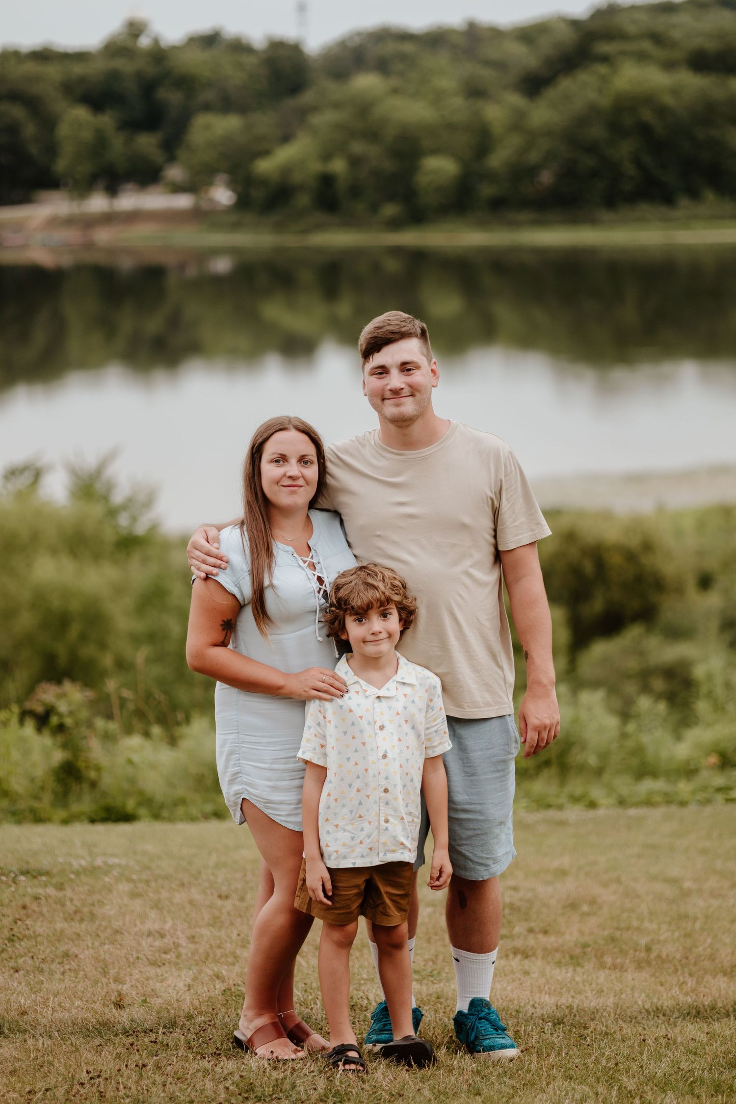 Three people pose for a casual portrait by a lakeside on a summer day.
