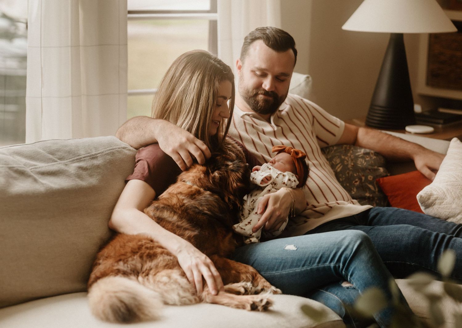 Family relaxes on couch with their golden retriever dog in cozy living room setting.