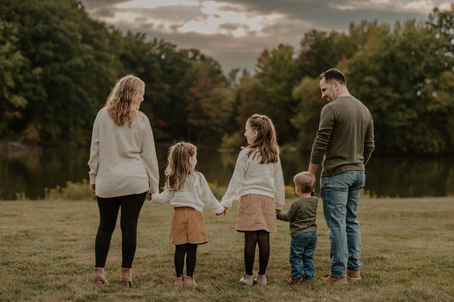 A family of five holding hands while standing in a field at sunset.