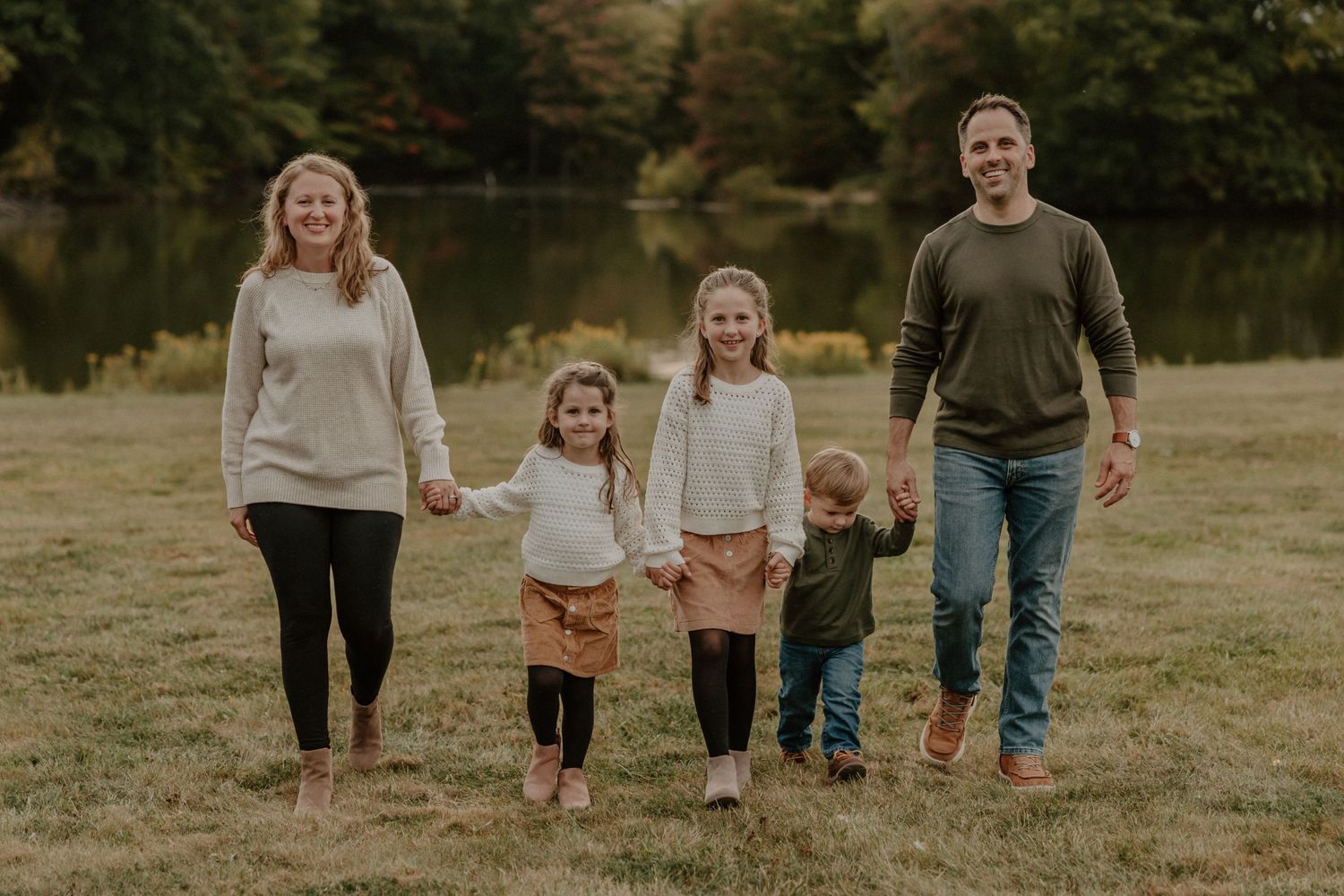 A family walks together through an autumn field near a lake.