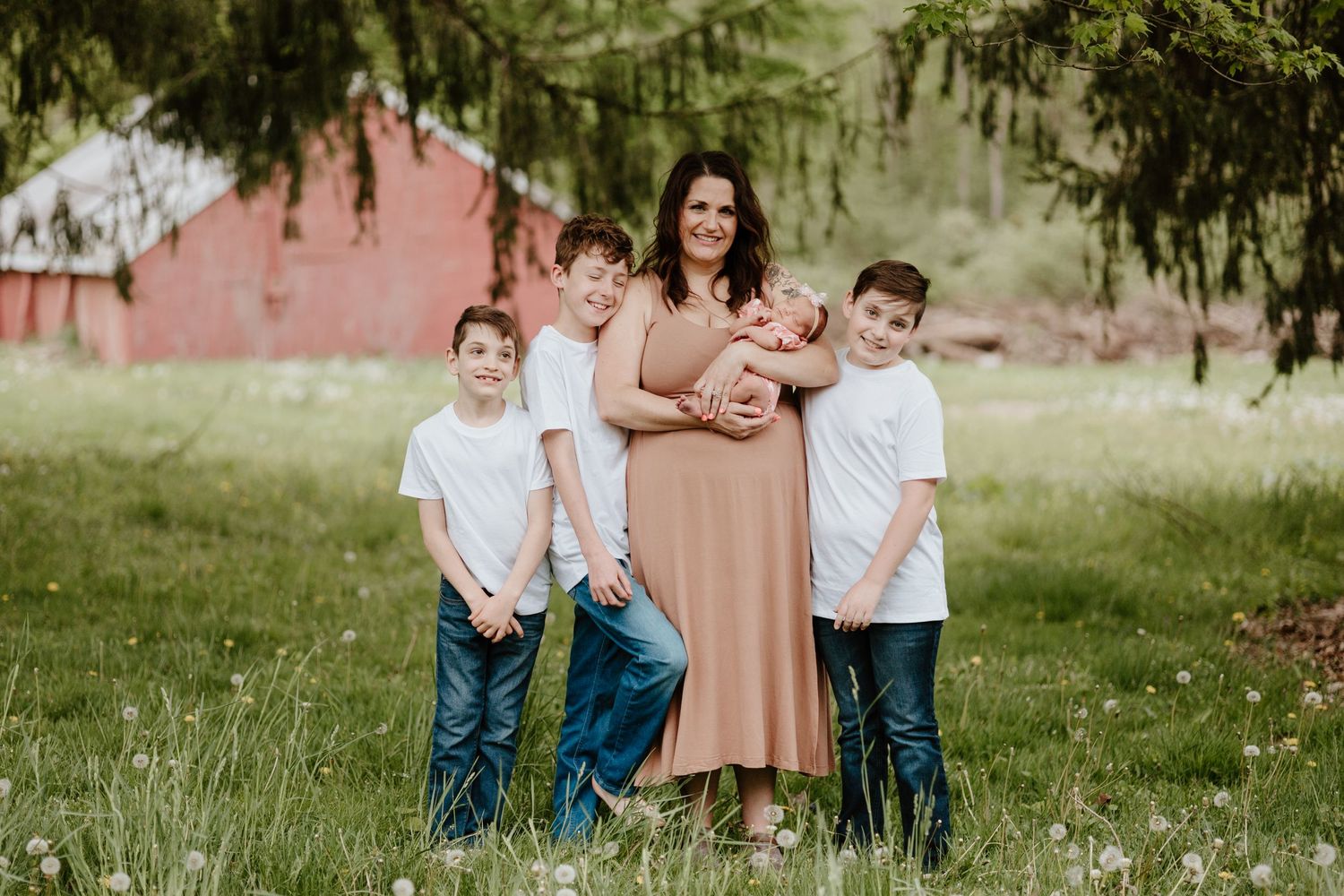 A family group stands together in a grassy field with a red barn in the background.