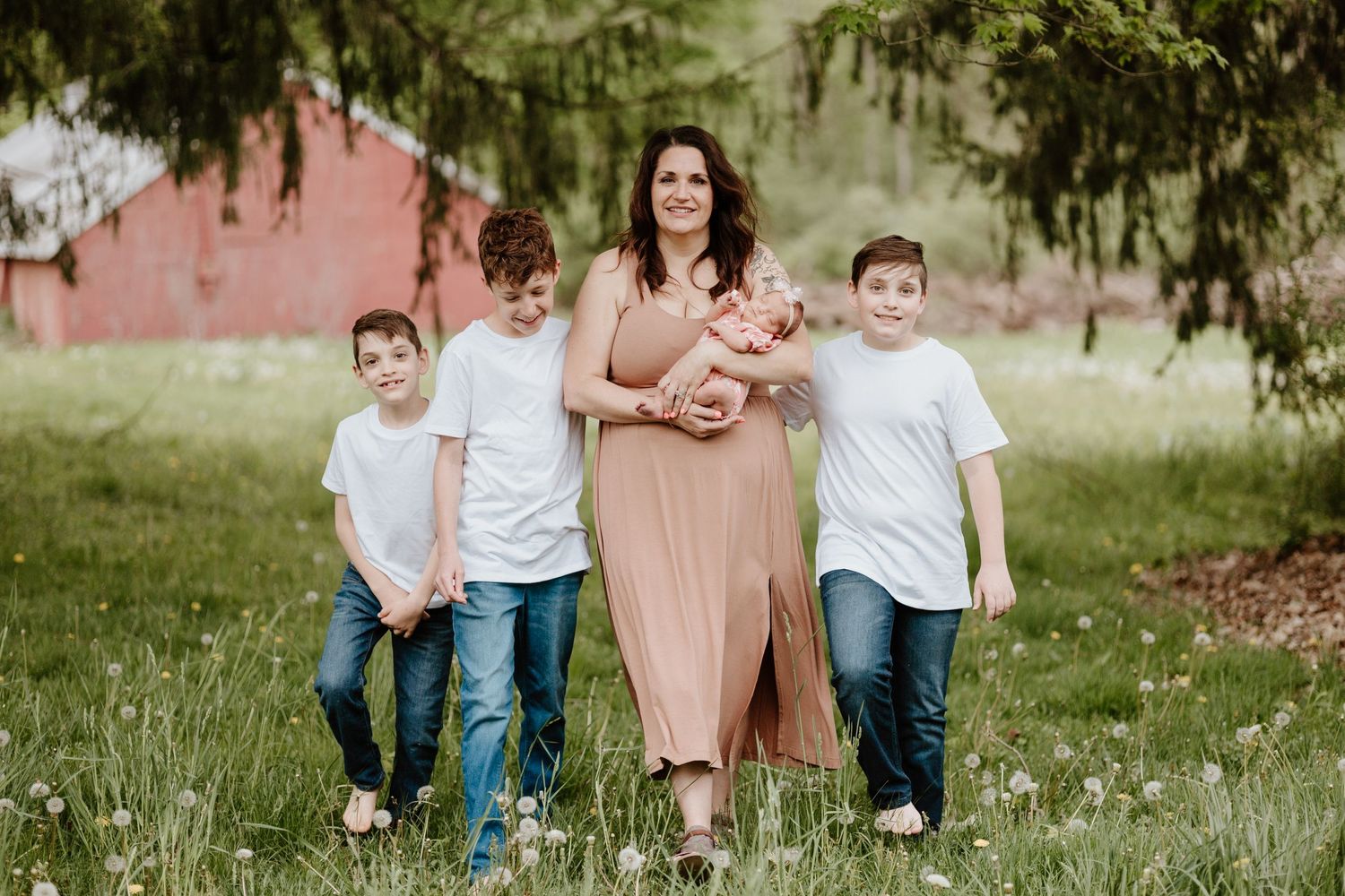 A family poses together on a spring day with evergreen trees and a red barn behind them.