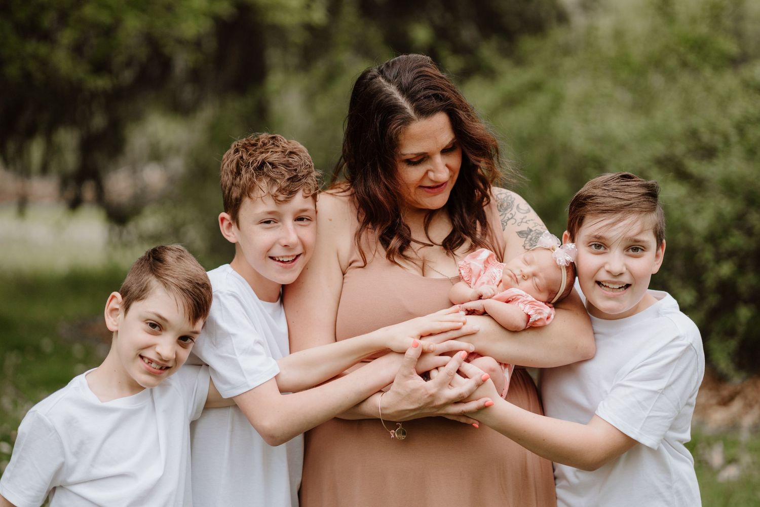 A loving outdoor portrait of siblings gathered around a precious newborn.