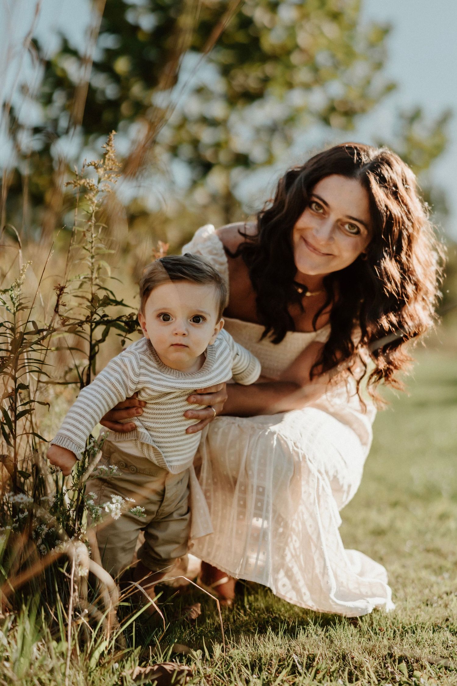 A mother and baby explore nature together during a sunset photoshoot in a meadow.