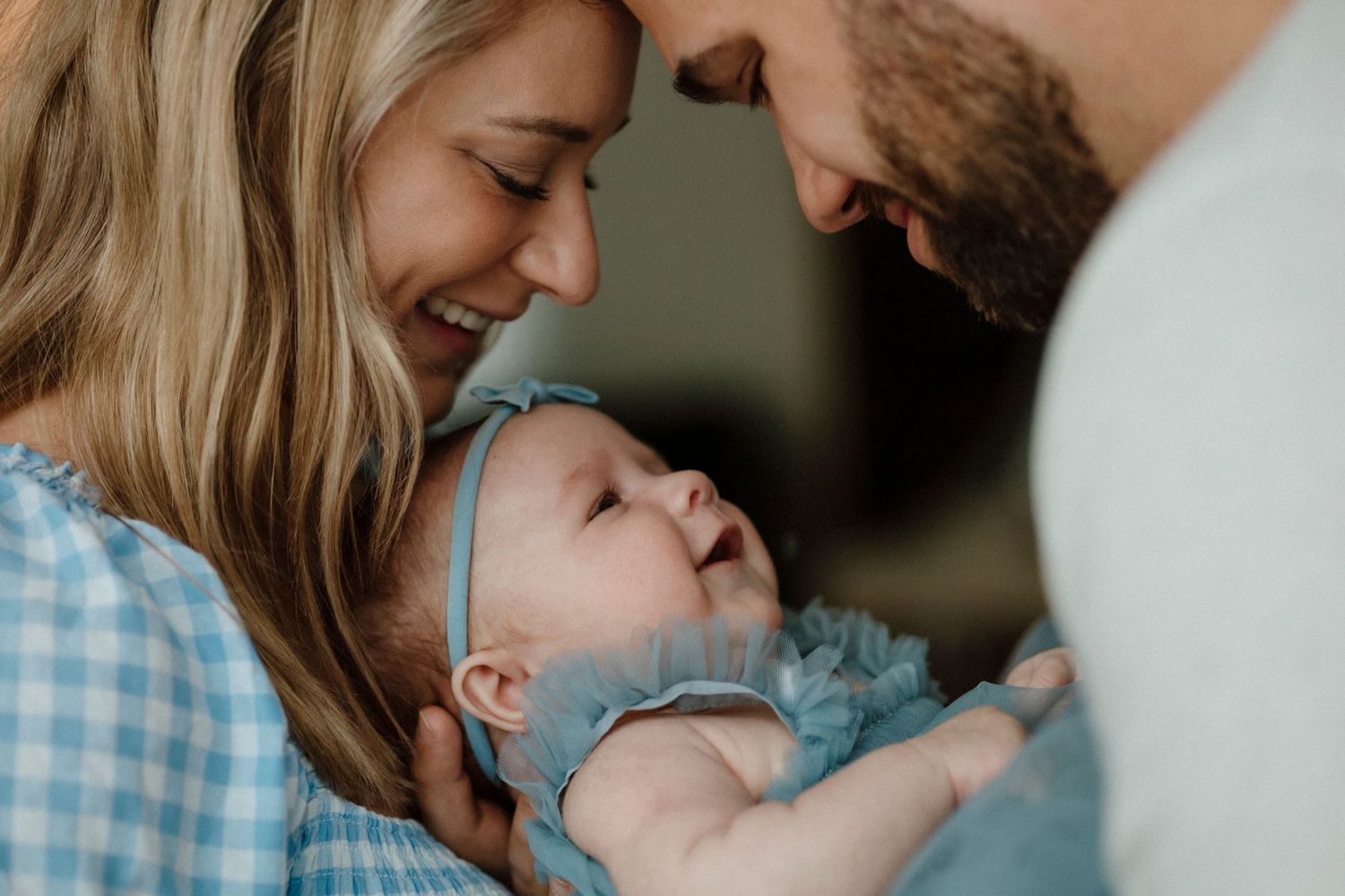 Tender family moment with baby in blue outfit and parents sharing a close embrace.
