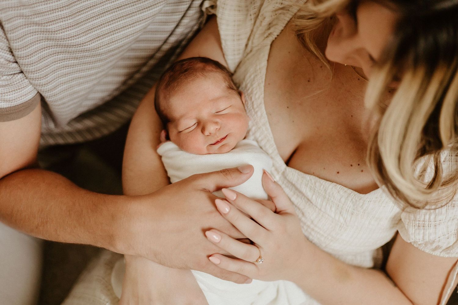 Close-up of sleeping newborn being cradled gently in parents' hands.