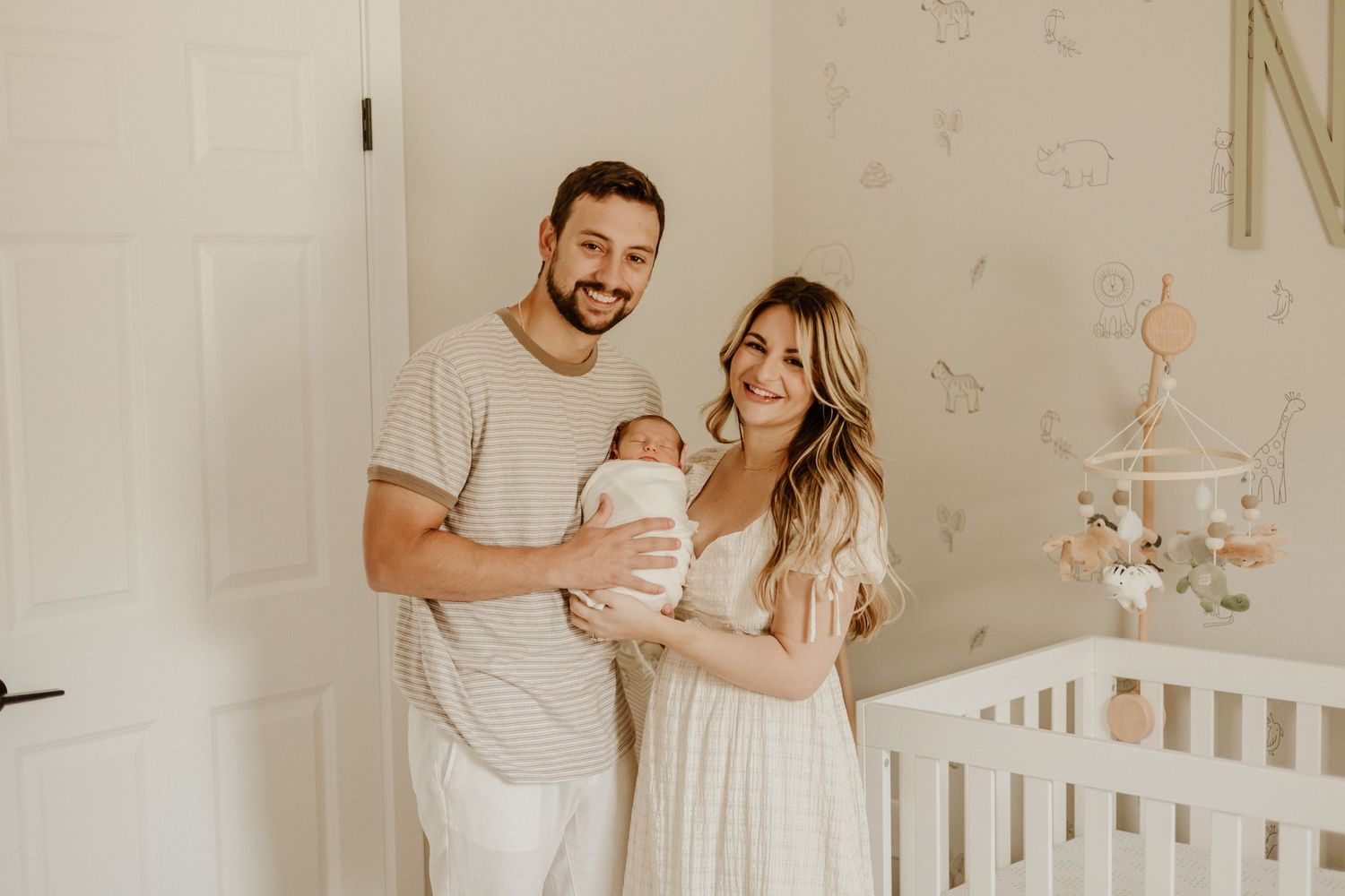 Parents stand in nursery decorated with butterflies while holding their newborn baby.