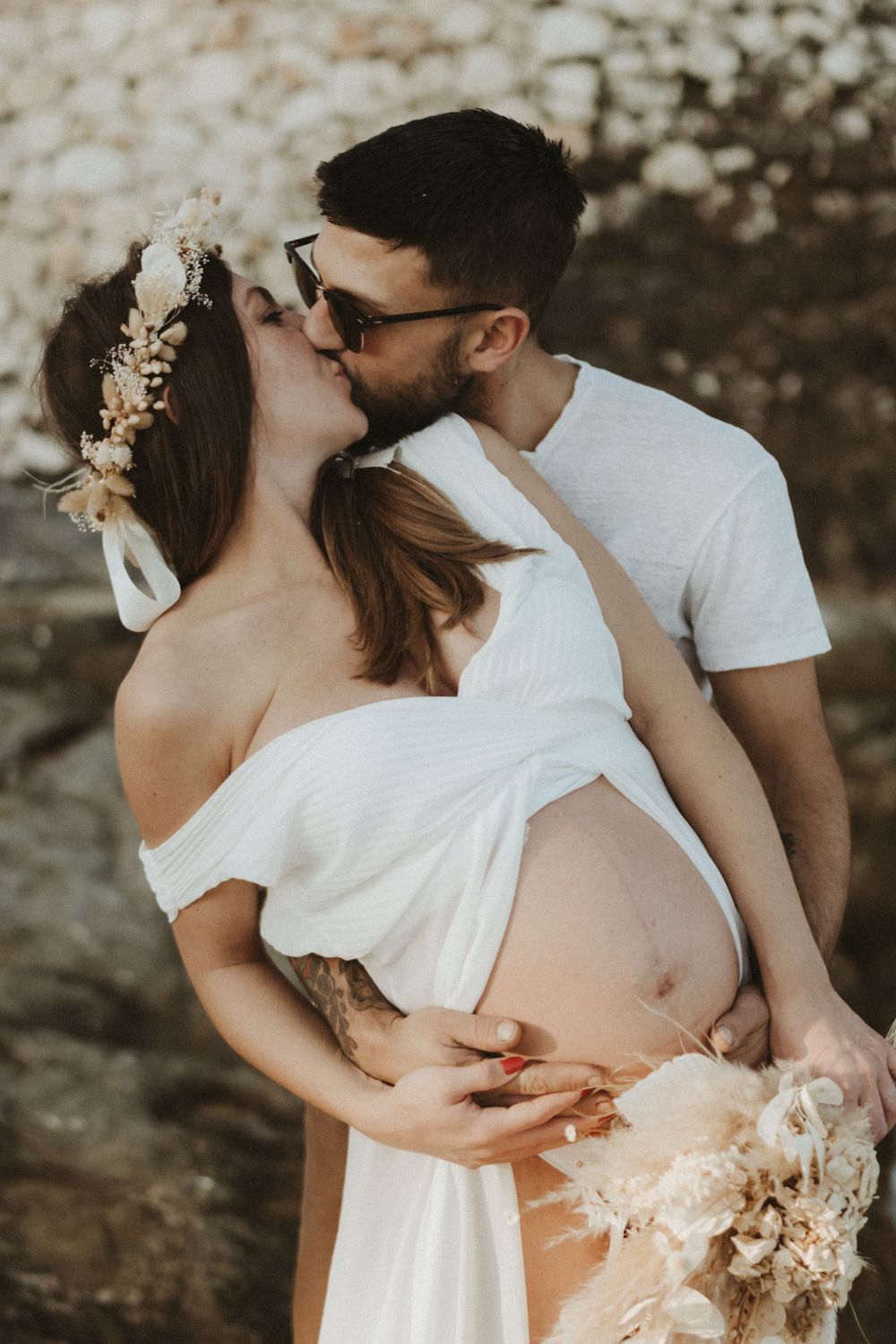Romantic maternity portrait with floral crown and white dress against natural backdrop.
