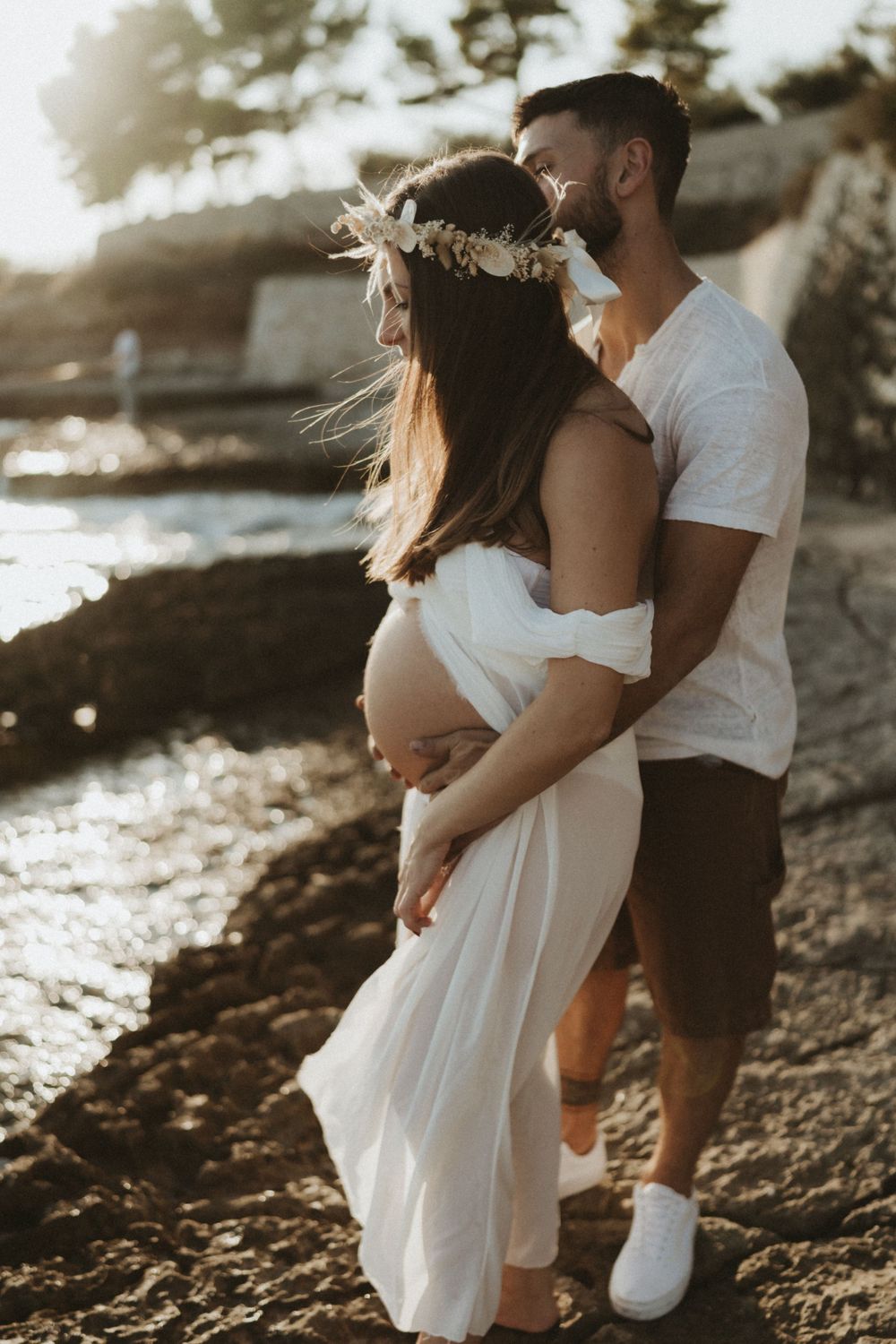 Romantic beachside maternity photoshoot with couple in white clothing at golden hour.