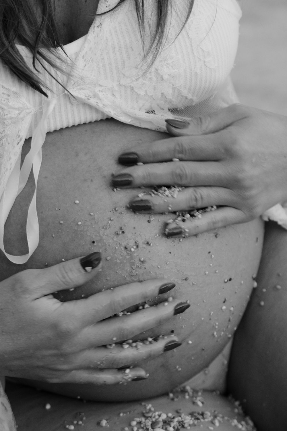 Black and white close-up of glitter-covered pregnant belly with hands gently resting.