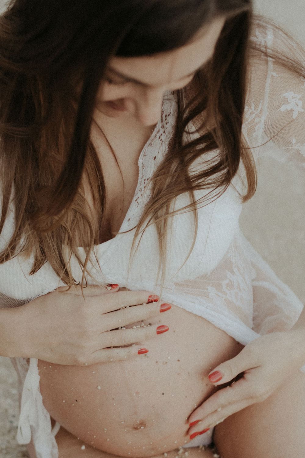 Artistic maternity photo with soft lighting showing pregnant belly and red painted nails.
