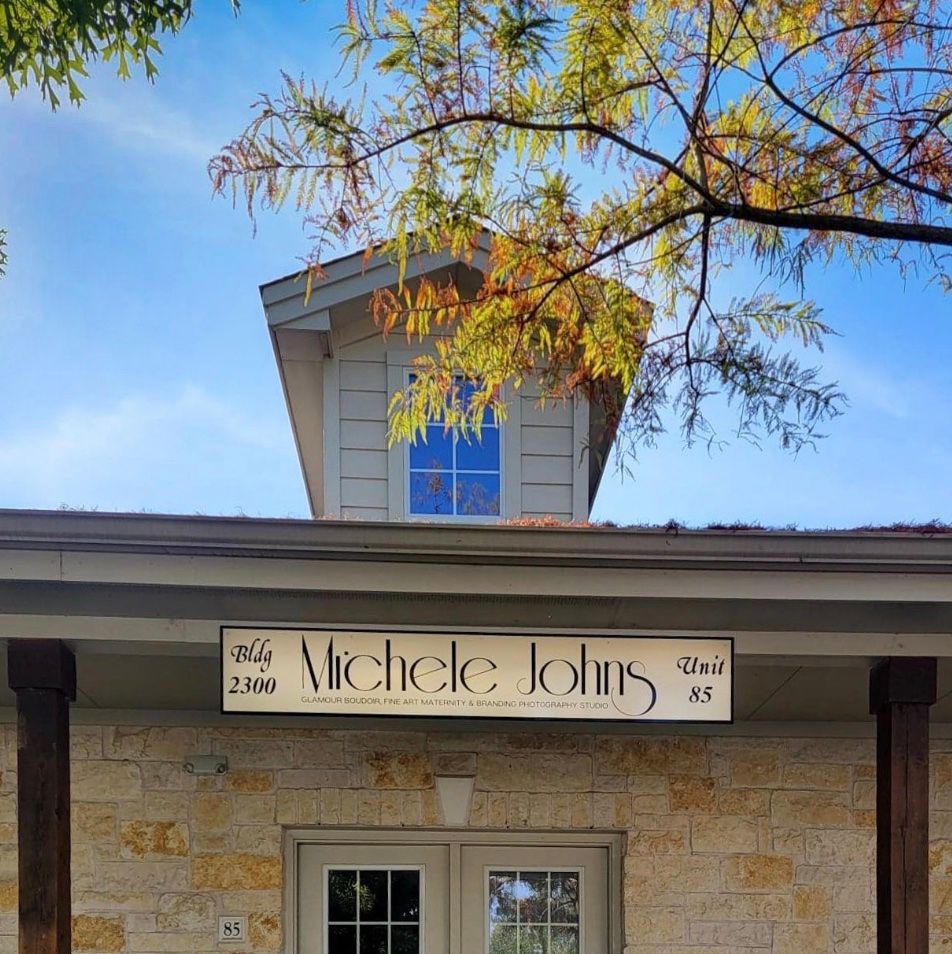 Stone facade building entrance with Michele Johns sign and decorative fall foliage.