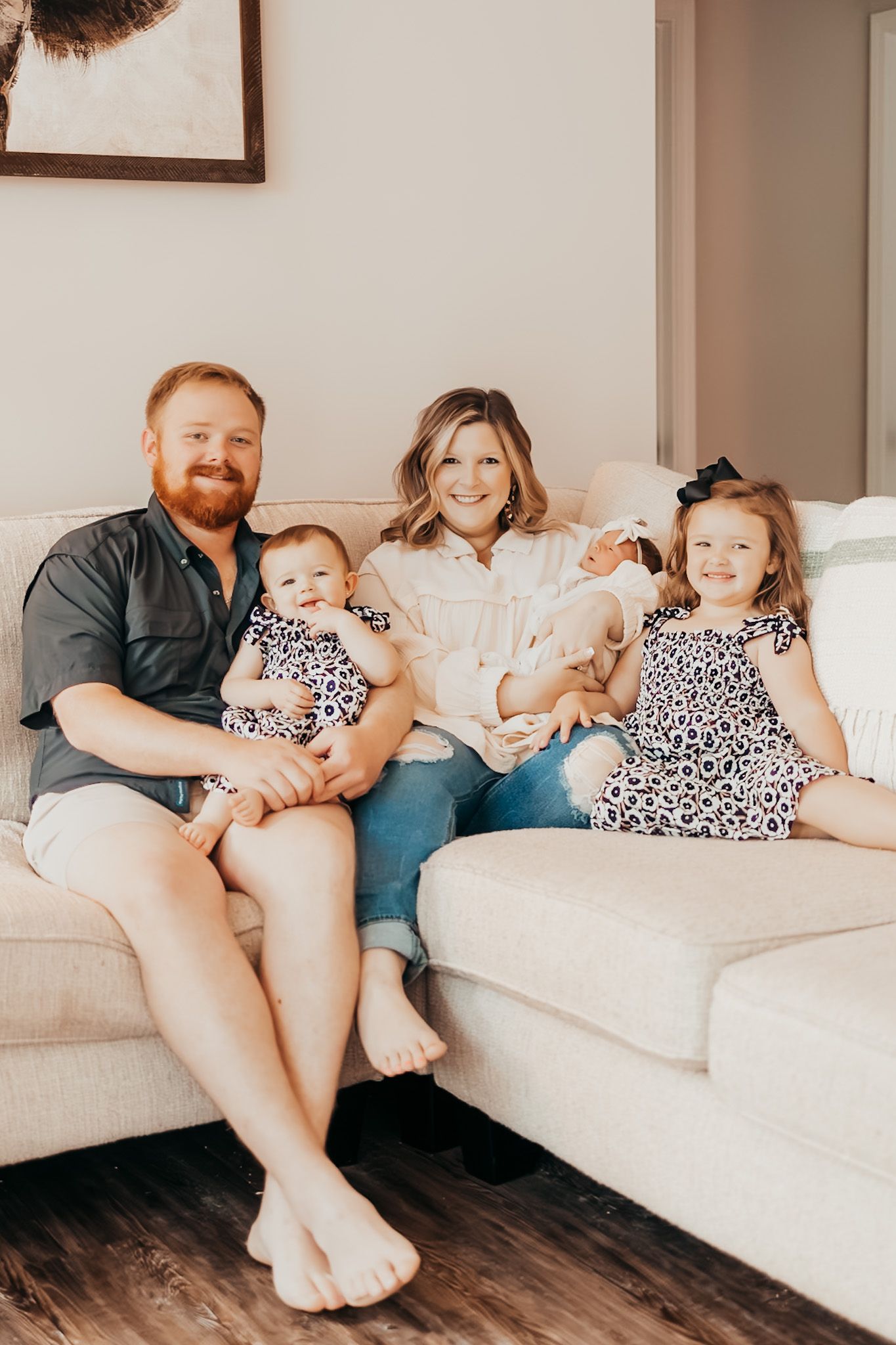 mom dad and two kids sitting on the couch with their two matching daughters and their newborn baby