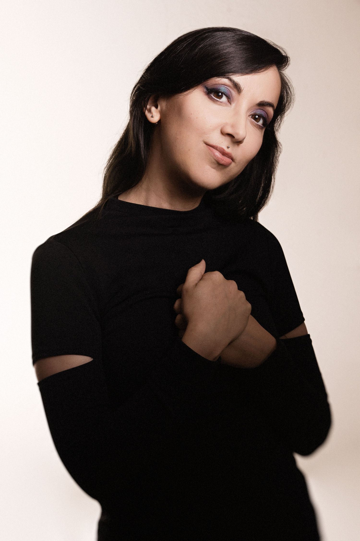 Fashion portrait in black turtleneck with cut-out sleeves against neutral background.