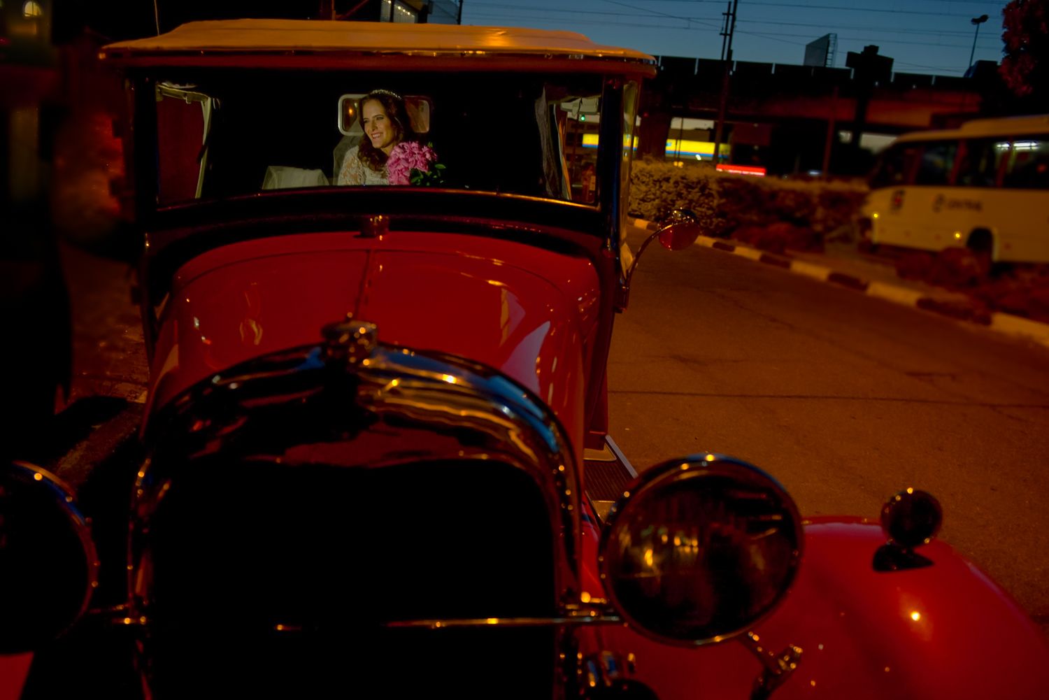 Classic red vintage car photographed at night with street lights in background.