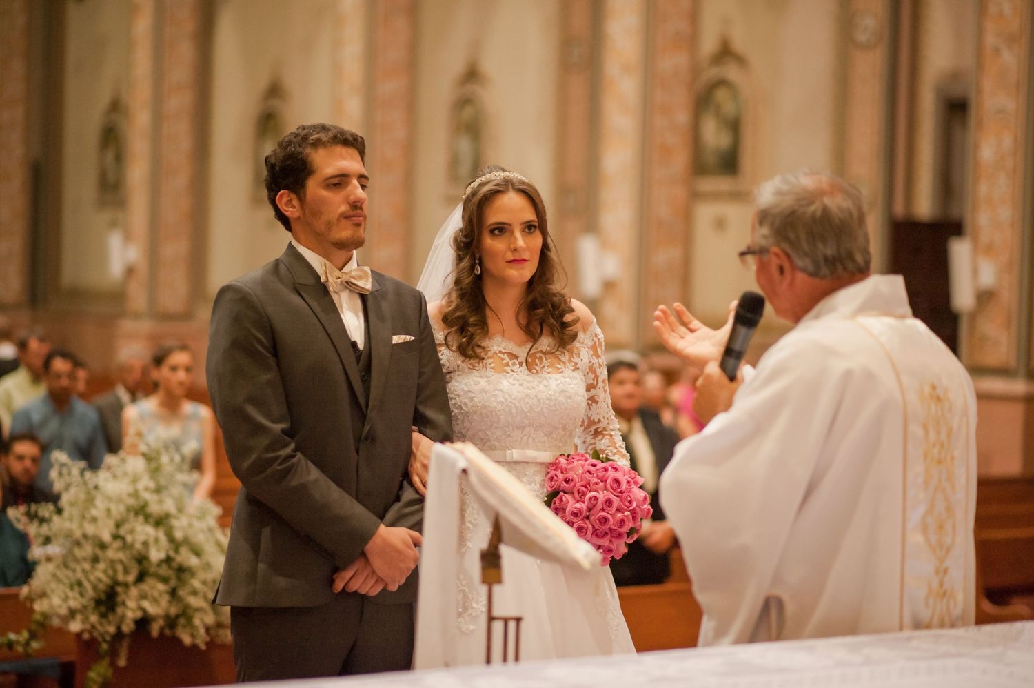 Wedding ceremony in progress with couple and priest at ornate church altar.