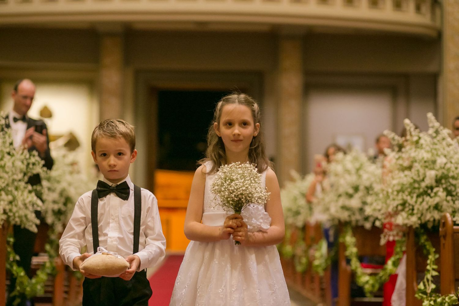 Young ring bearer and flower girl walk down the church aisle during wedding ceremony.