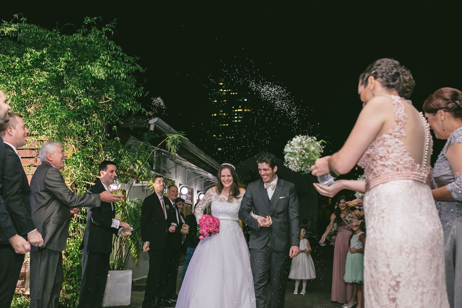 Wedding party celebrates during outdoor ceremony with guests blowing bubbles at dusk.