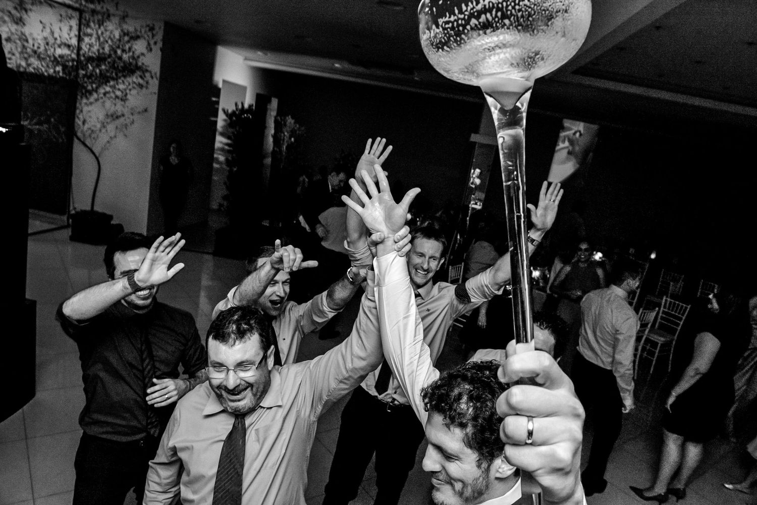 Party guests celebrate on dance floor with raised drinks and hands.