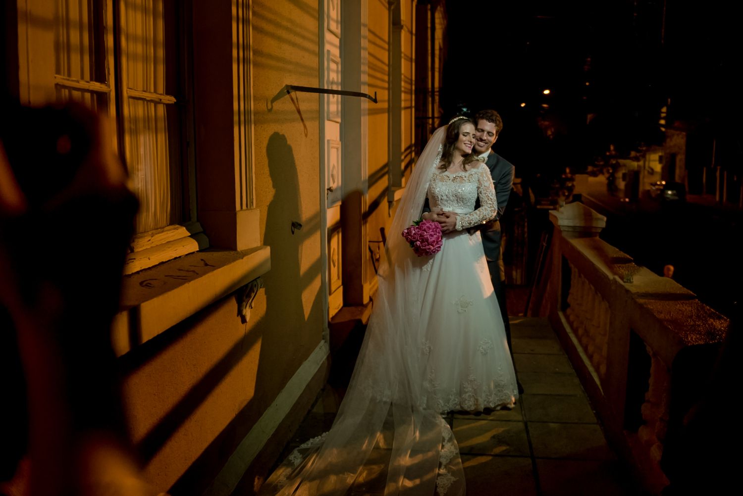 Couple embraces against illuminated building facade at night.