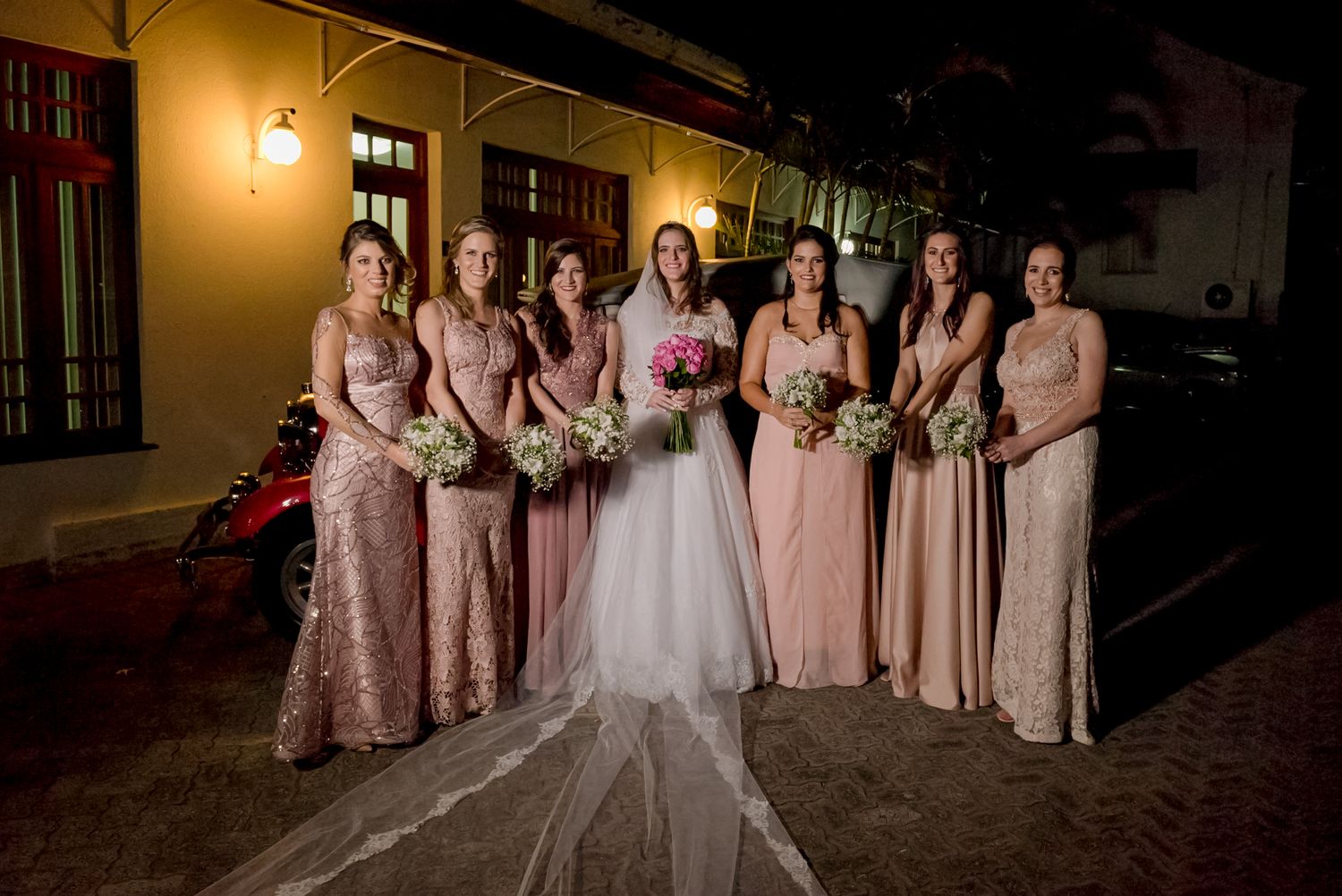 Wedding party in blush pink and sparkly dresses pose together at nighttime on a cobblestone street.