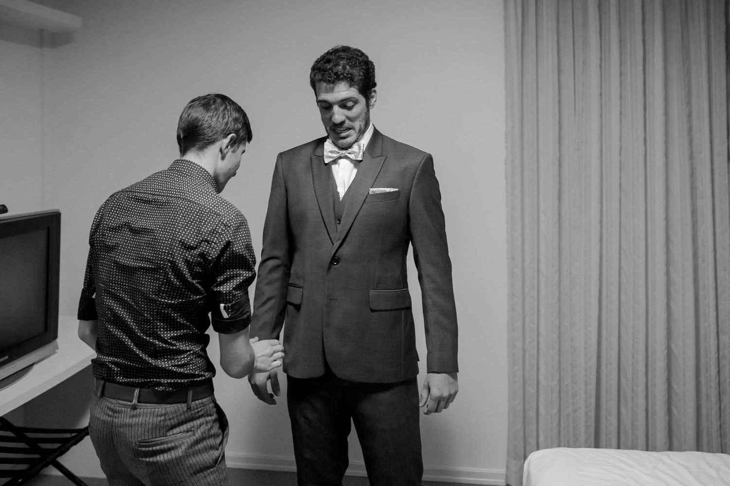 A groom receives final adjustments to his suit in black and white.