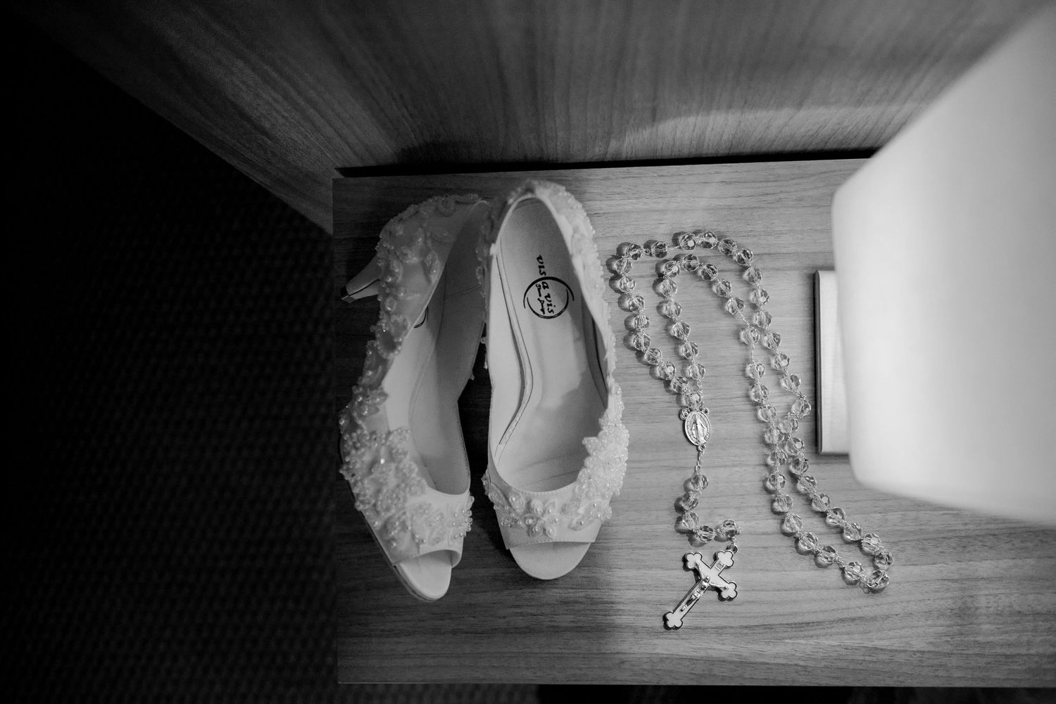 White bridal shoes and crystal jewelry arranged on wooden flooring in monochrome.