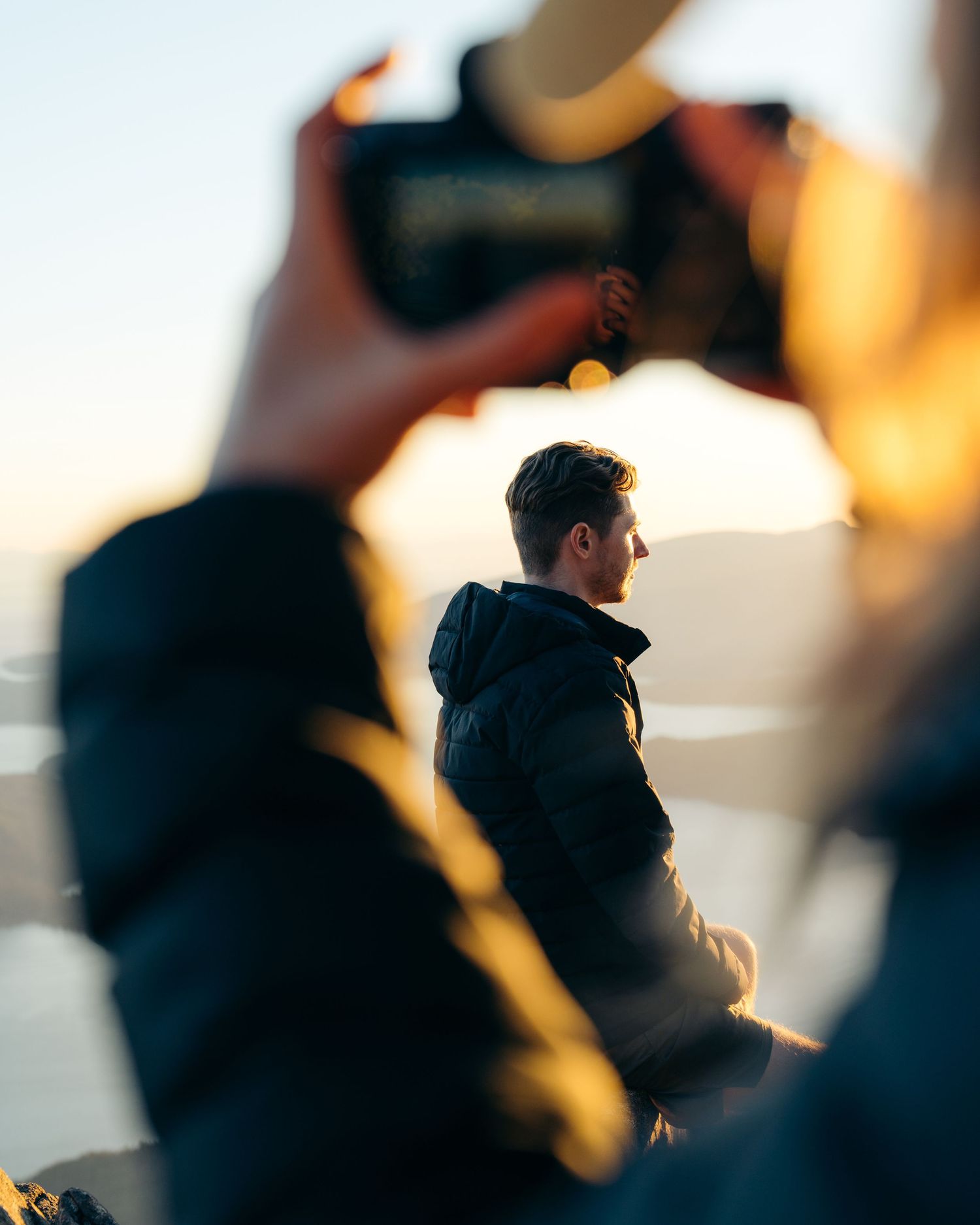 Silhouette of someone wearing a dark hoodie against a blurred, warm-toned background at sunset.