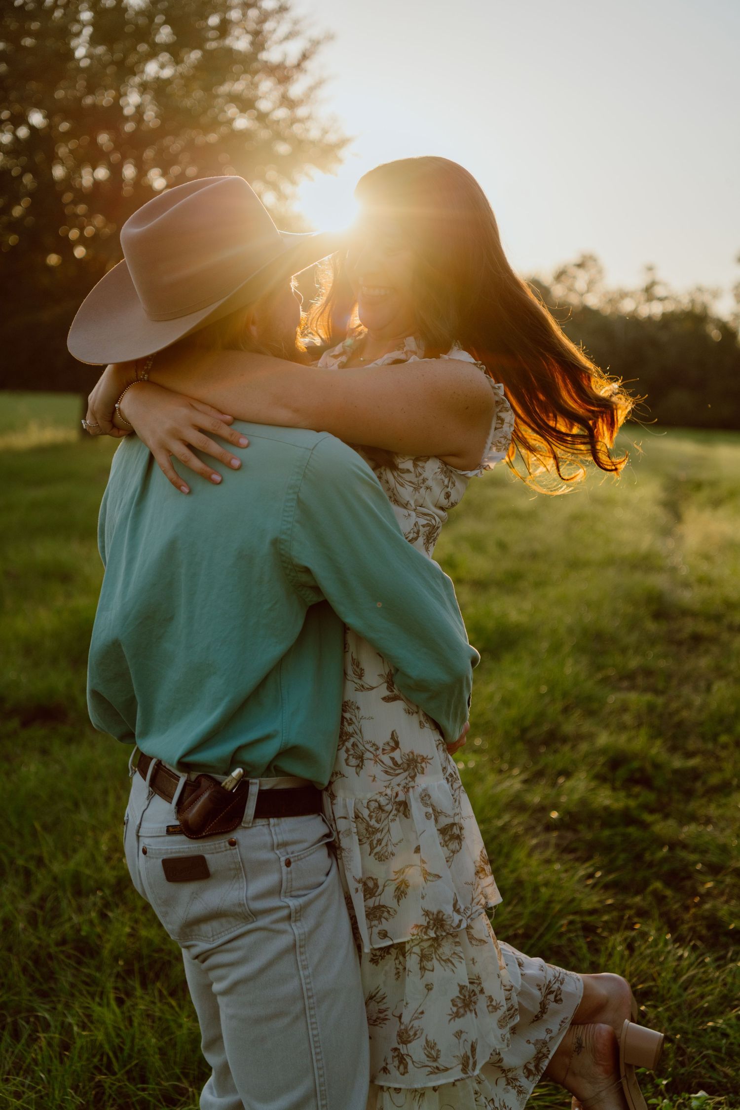 A couple laughs and embraces in casual attire against a white wall.