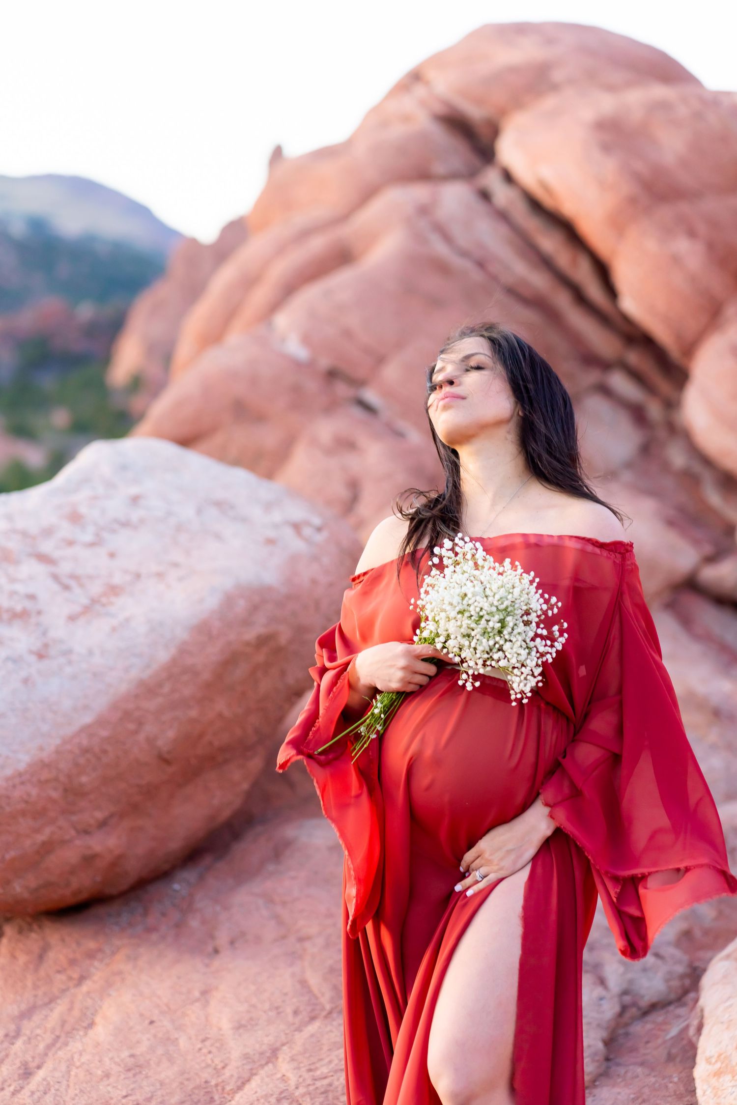 A flowing red dress adorns a figure holding baby's breath flowers against dramatic red rock formations.