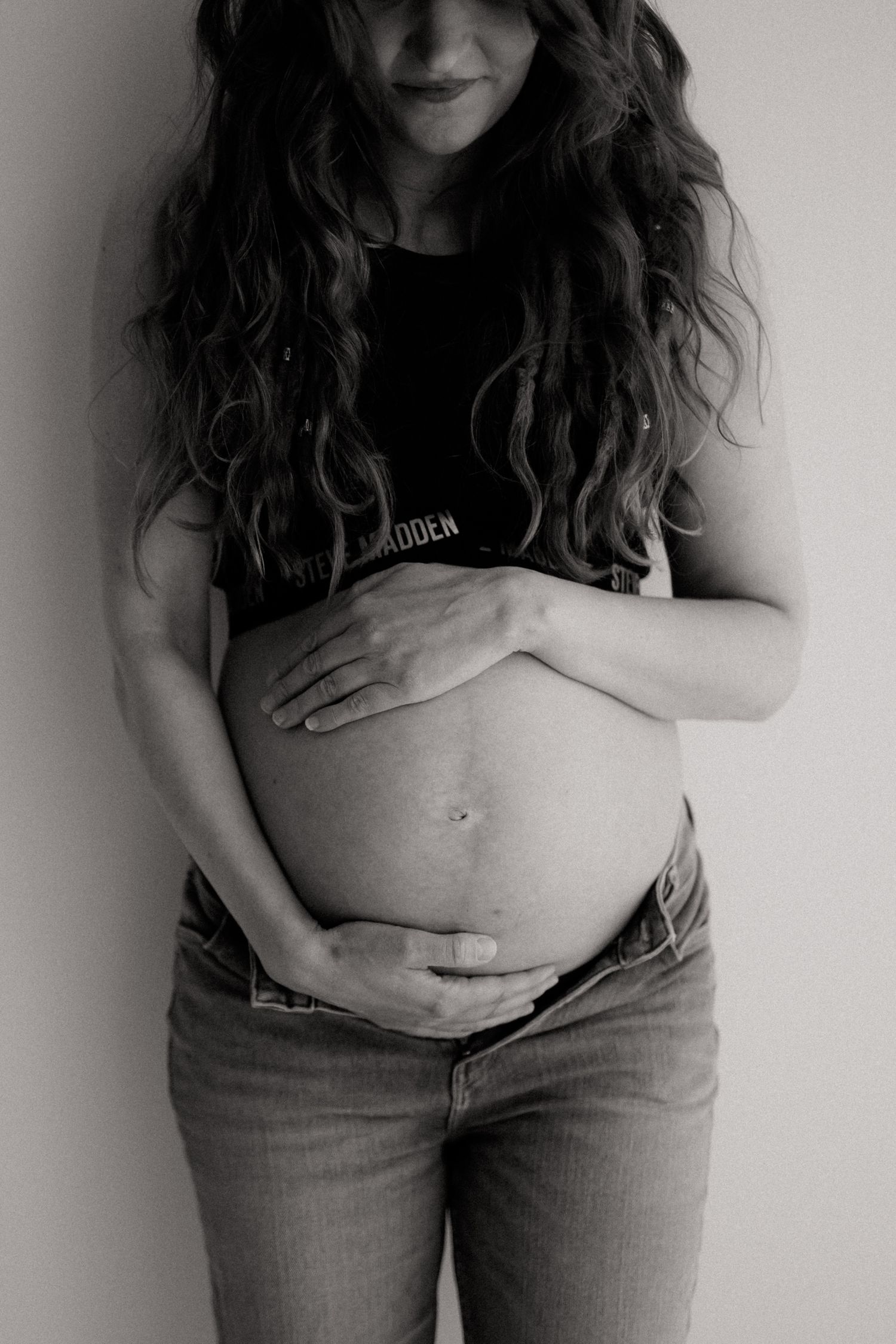 Expecting mother in pink sweater holding purple flowers against her pregnant belly.