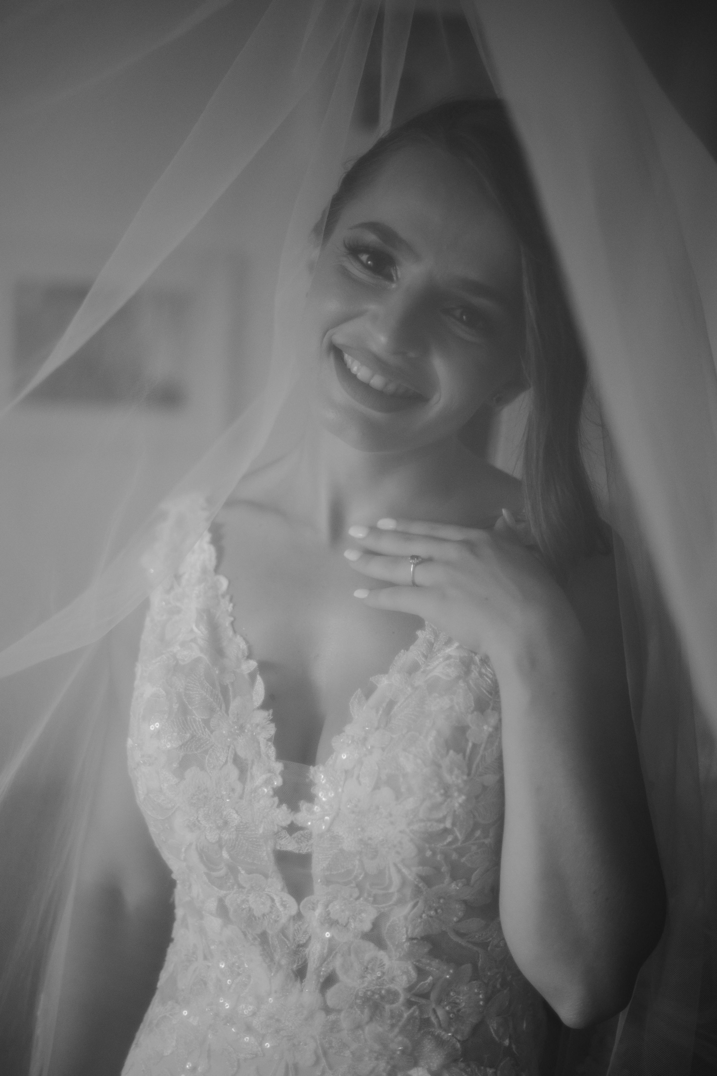 A romantic black and white bridal portrait shows a joyful smile beneath a delicate veil and lace wedding gown.