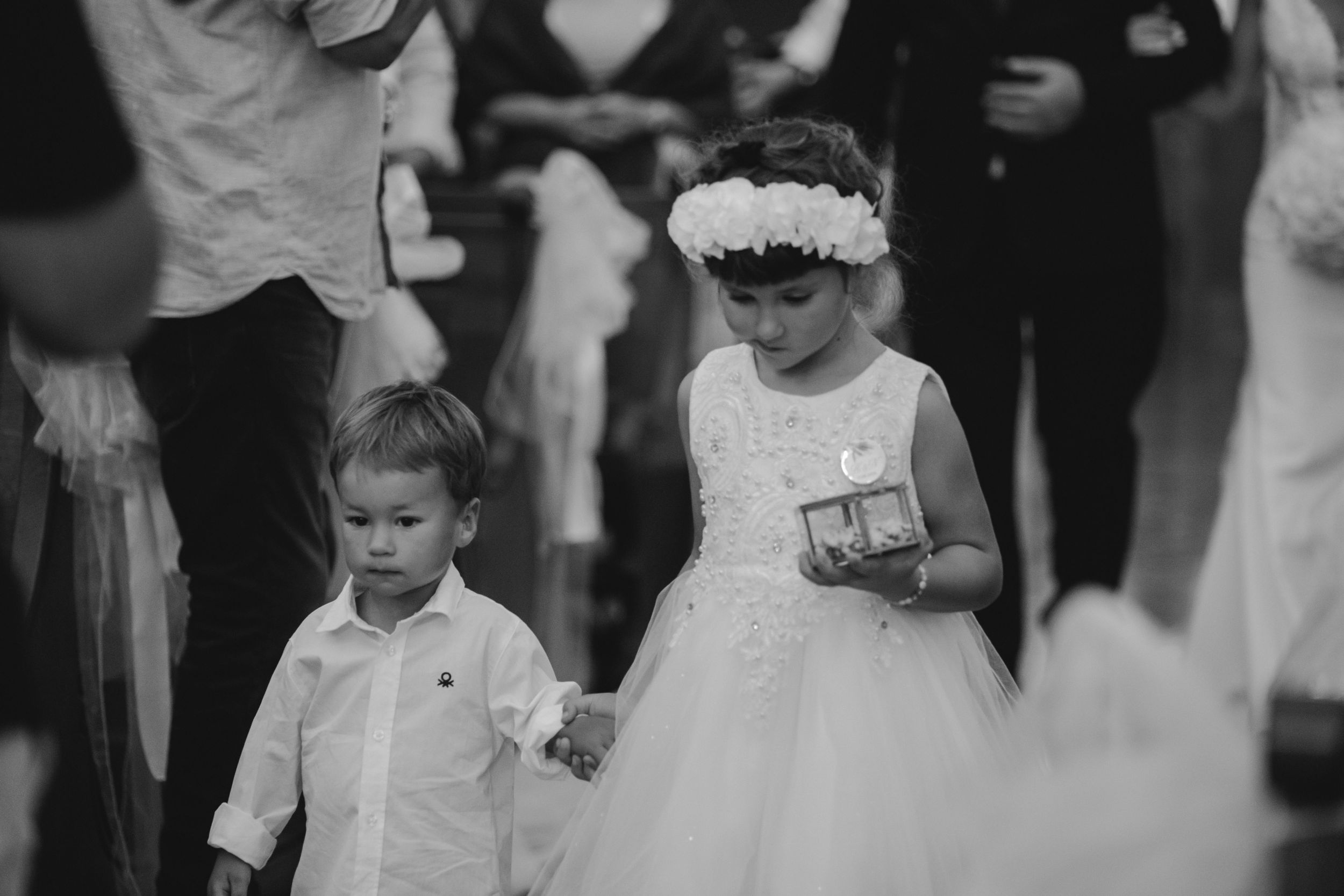 A young ring bearer and flower girl walk together during a wedding ceremony.