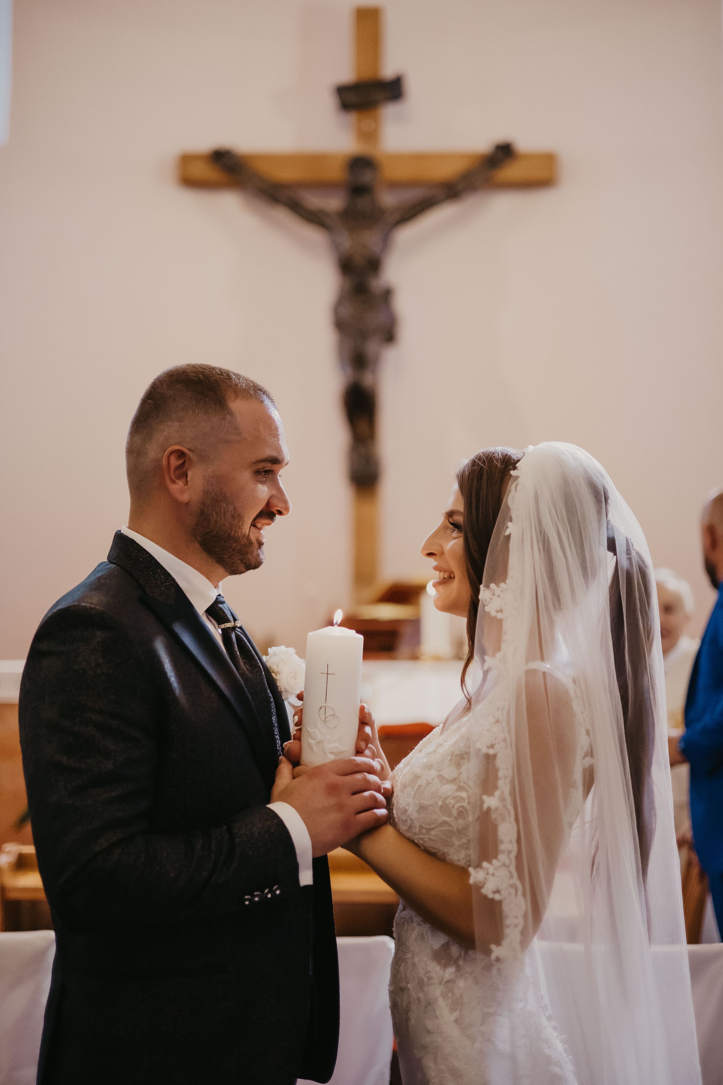 A couple shares a moment during their wedding ceremony while holding candles beneath a crucifix.
