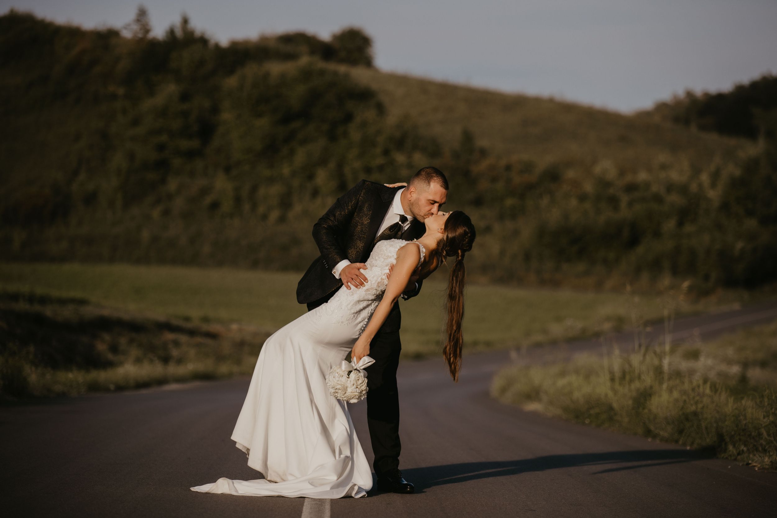 A dramatic dip pose between newlyweds on a rural road at sunset.
