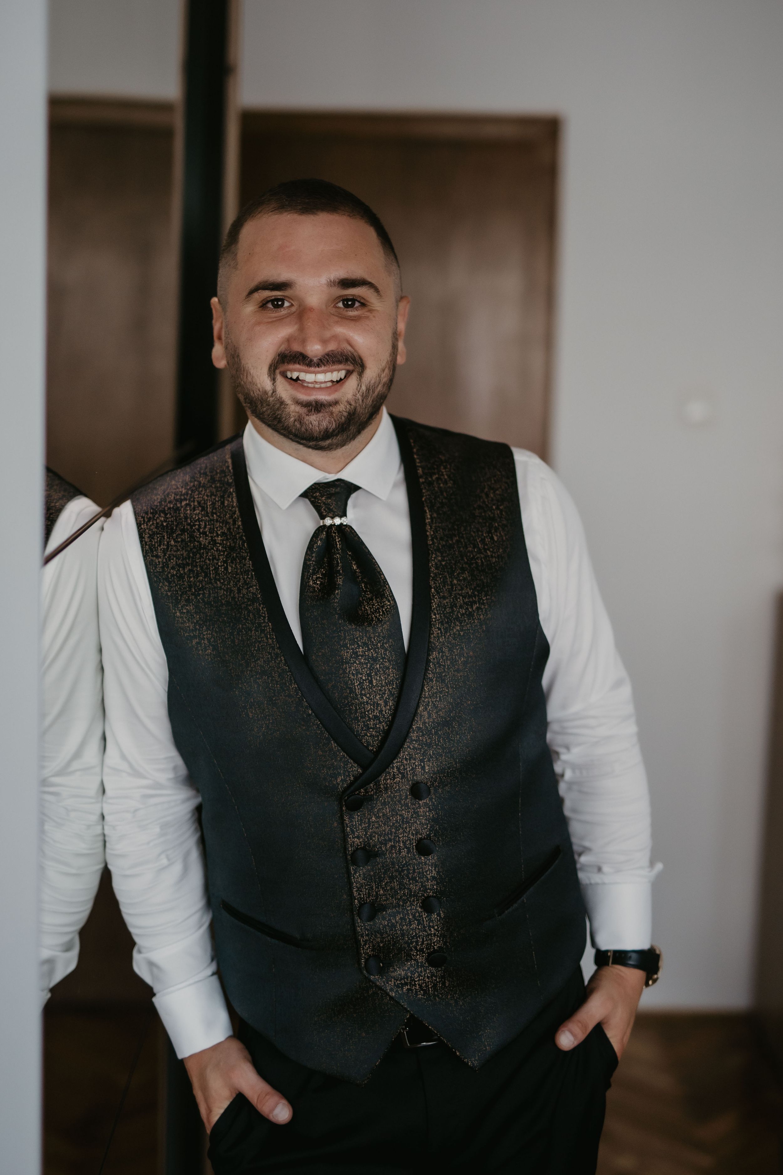 Groom in formal attire with sparkly vest smiling in indoor setting.