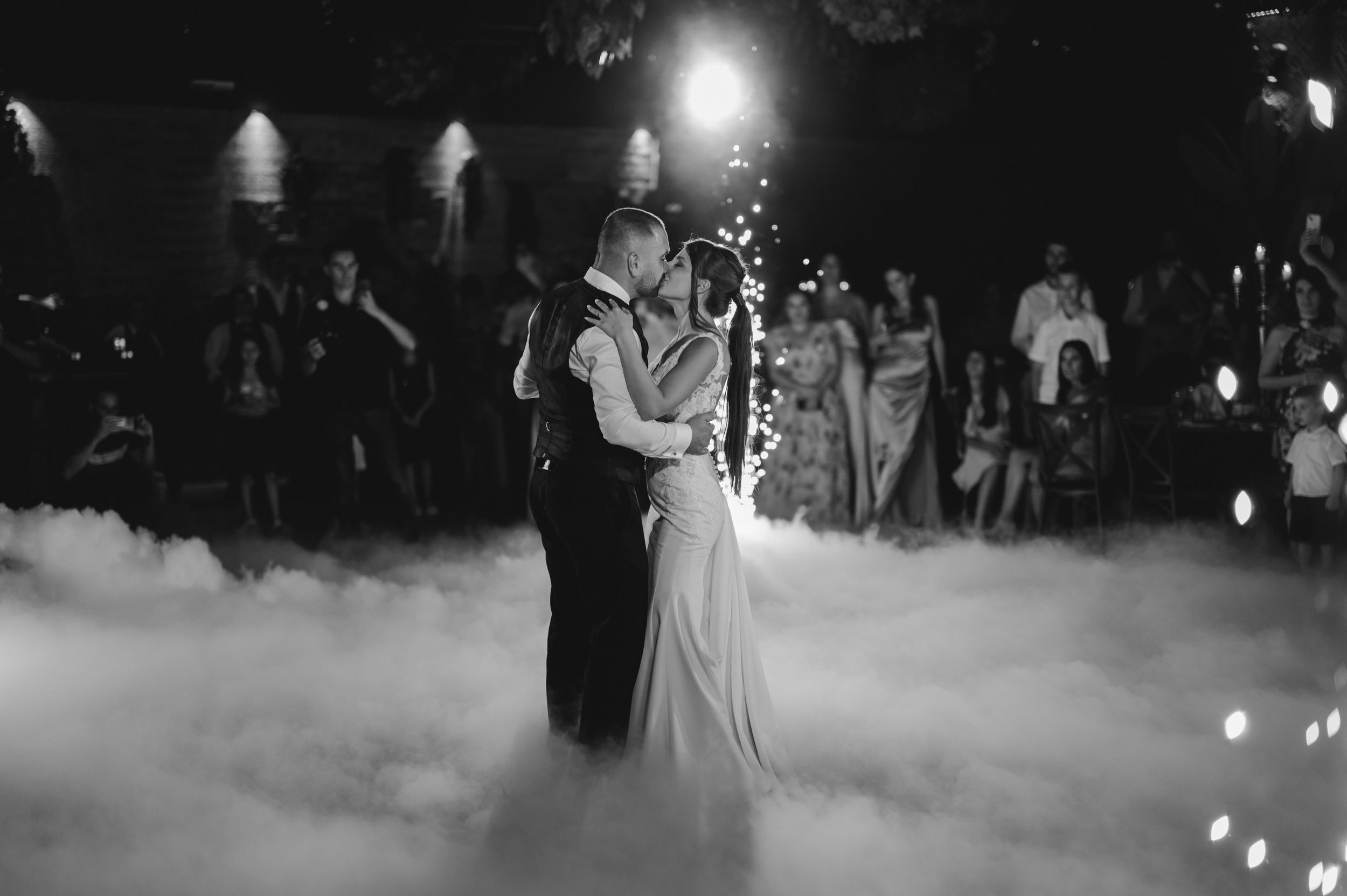 Couple shares their first dance surrounded by fog effects and romantic lighting at wedding reception.