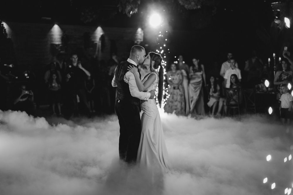 Couple shares their first dance surrounded by fog effects and romantic lighting at wedding reception.