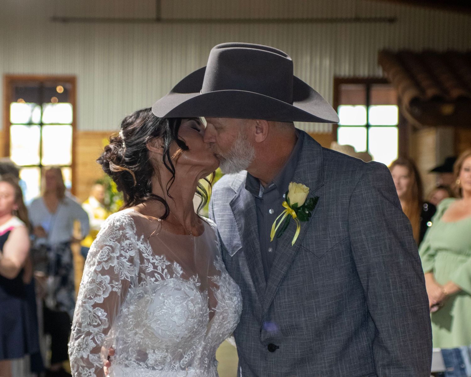 Intimate wedding moment capturing a romantic kiss between couple where one wears a lace dress and other a dark suit and cowboy hat.