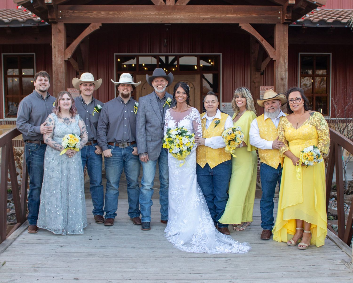 A wedding party in yellow dresses and denim stands together on a rustic wooden porch for a group photo.