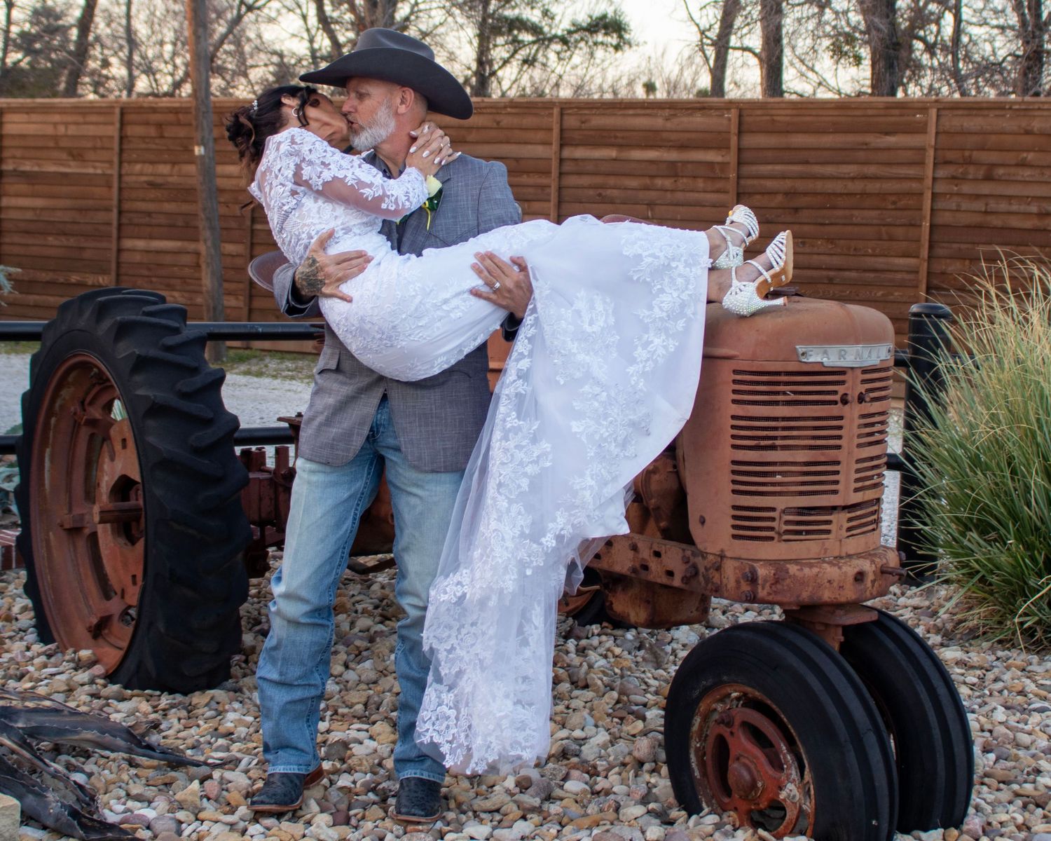 A romantic western-themed wedding photo with a couple posing by a vintage red tractor in golden sunlight.