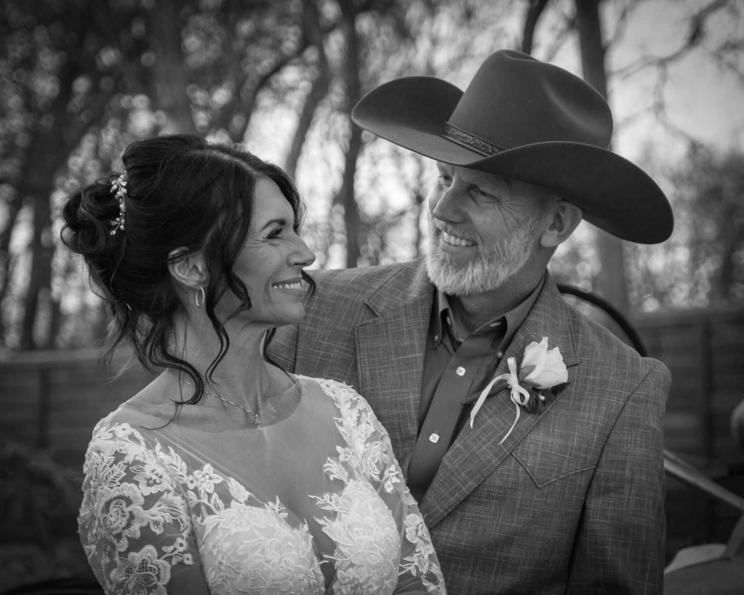 Black and white photo of a happy bride in a lace dress sharing a joyful moment with someone in a cowboy hat.
