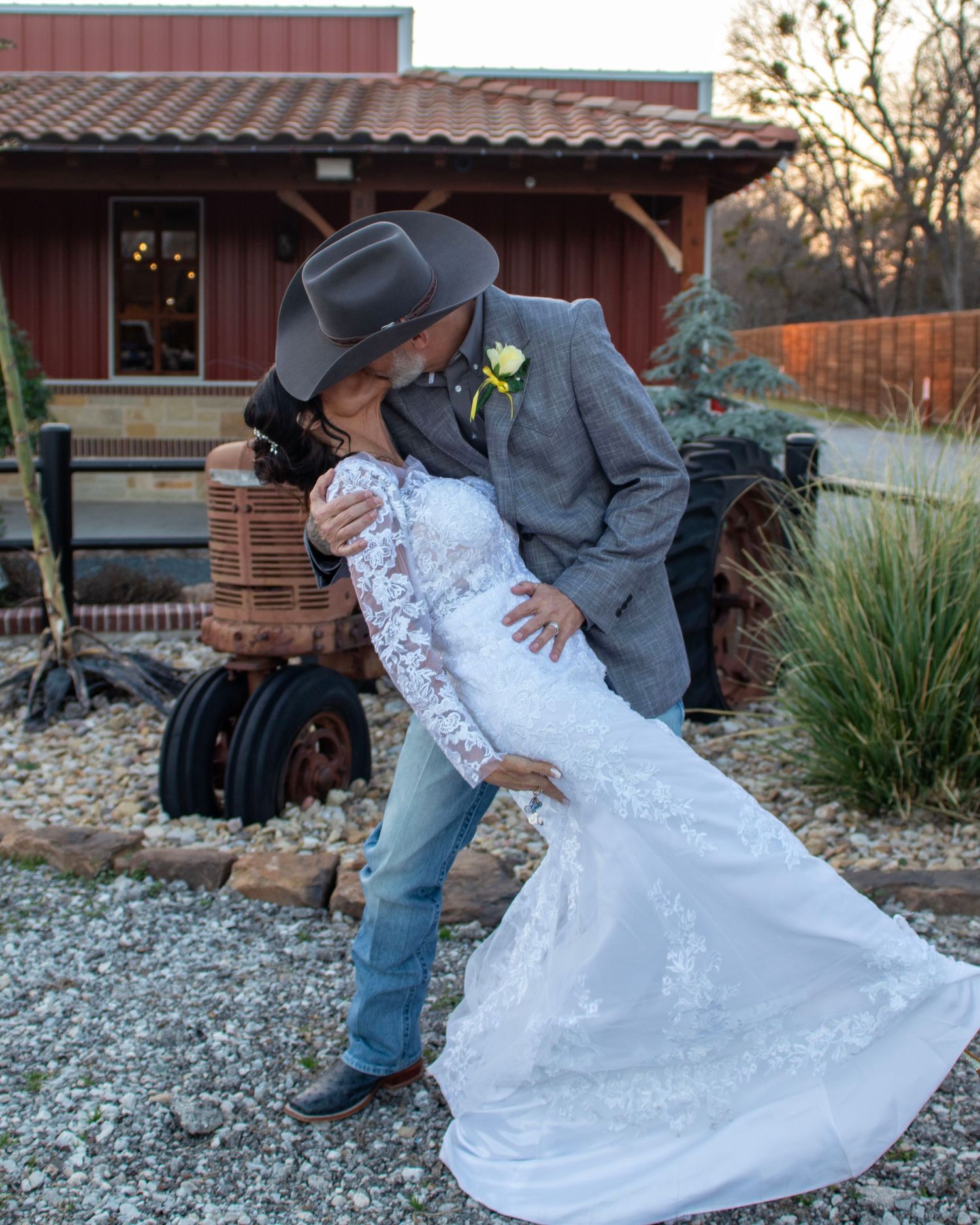 A romantic wedding pose against a rustic barn backdrop with cowboy hat and boots.
