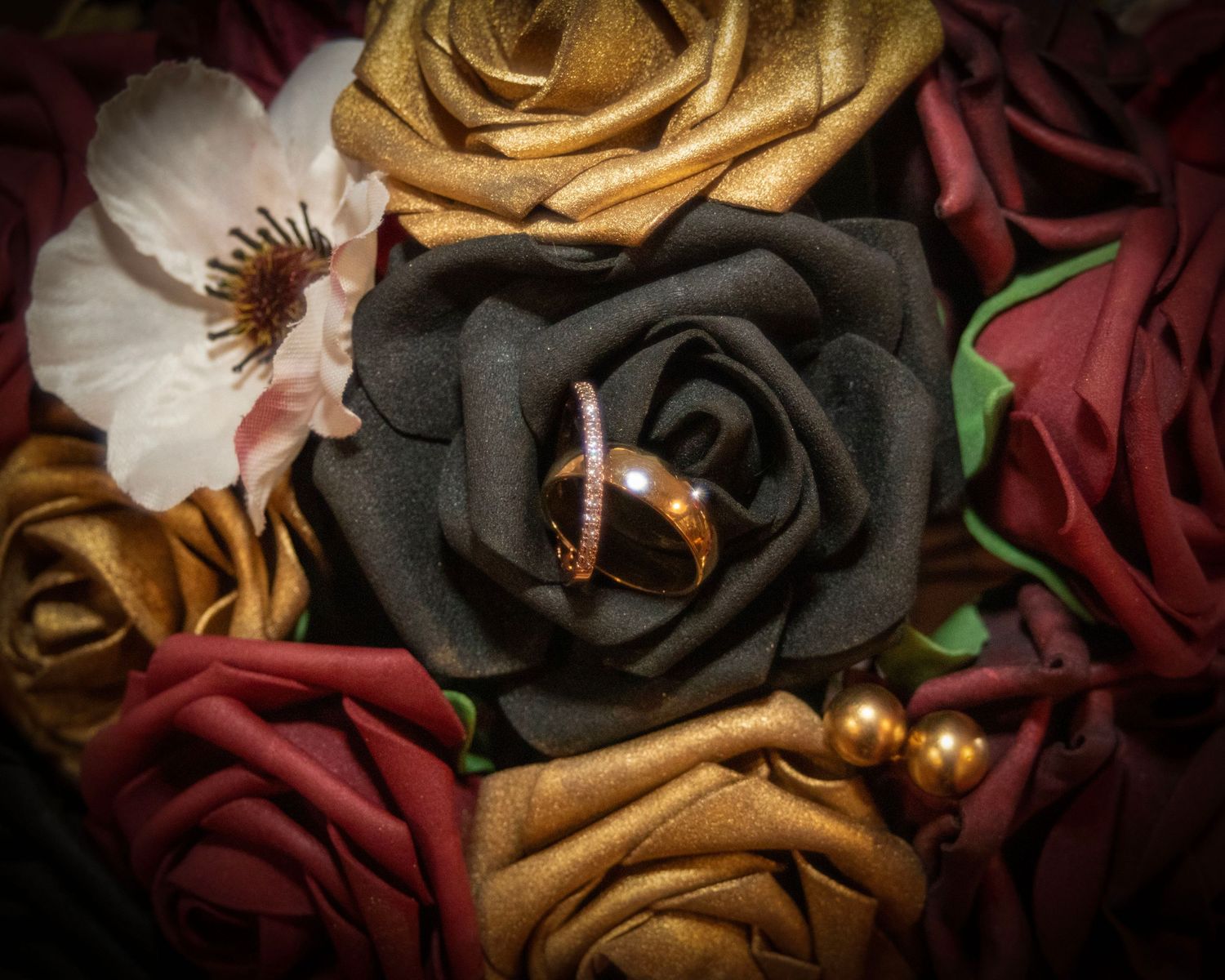Close-up of beautiful artificial roses in red, gold and black with a wedding ring nestled in a black rose.